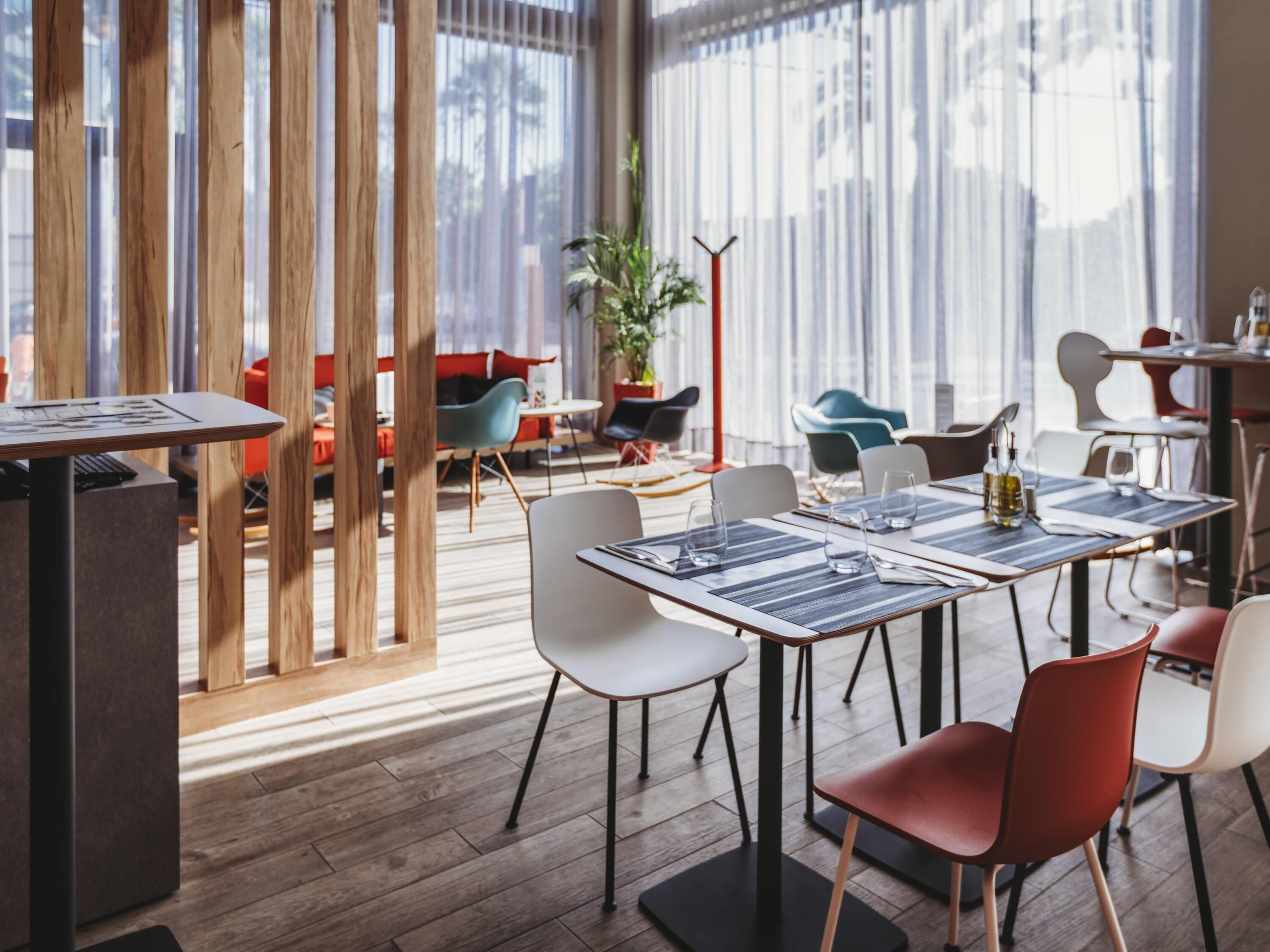 Un comedor moderno con separadores de madera, diversas opciones de asientos y un amplio ventanal que proporciona luz natural.