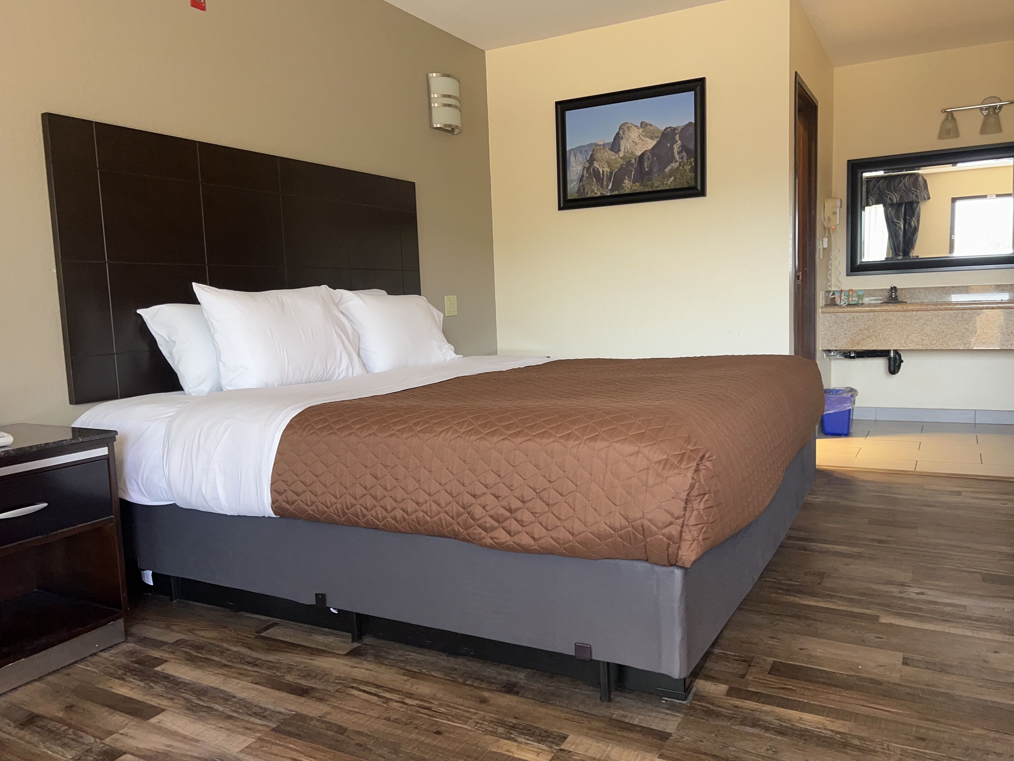Quarto de hotel com cama, mesa de cabeceira, banheiro com espelho e um quadro na parede.