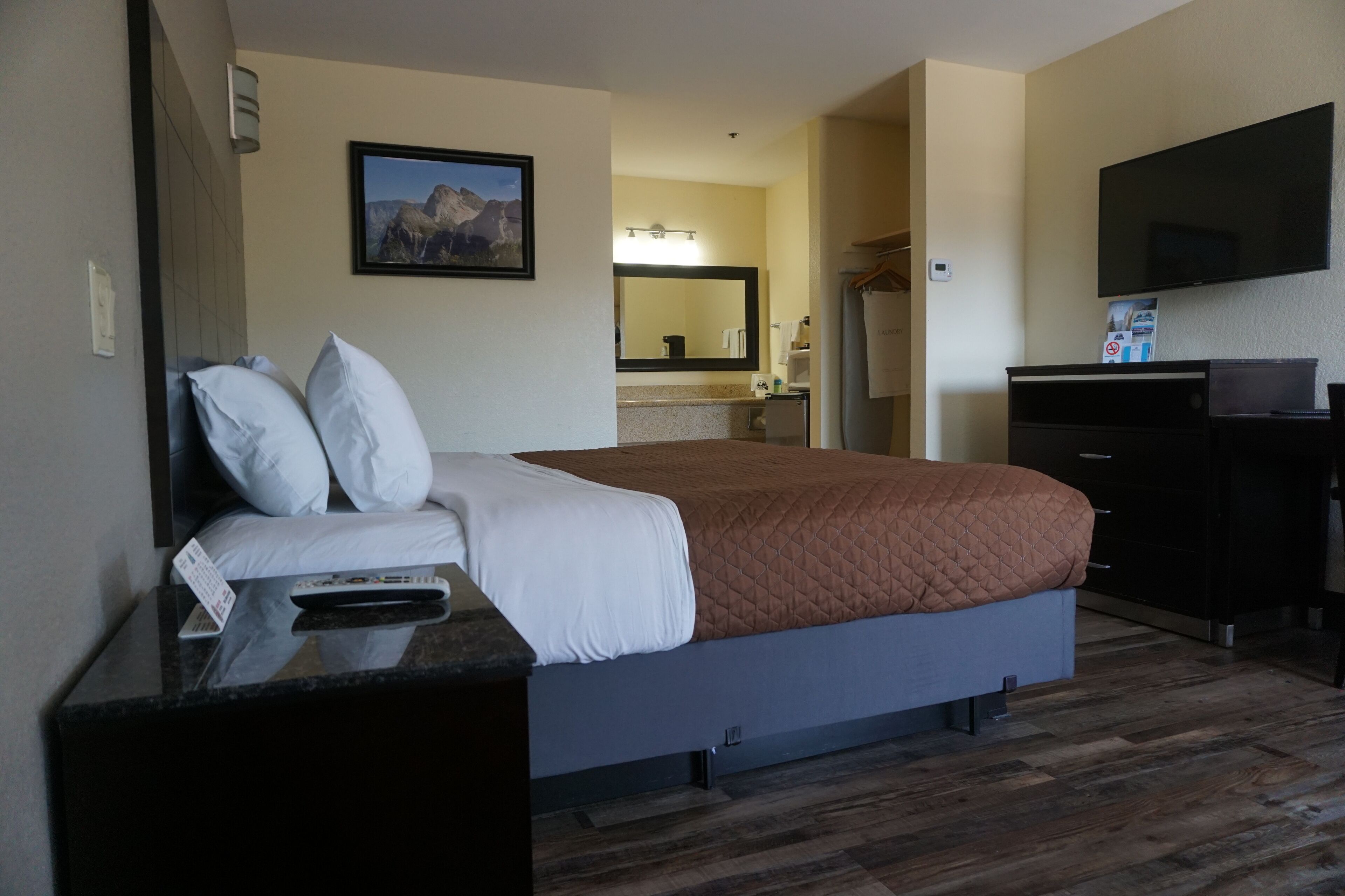 Ein Hotelzimmer mit einem Bett, einem Schreibtisch mit Fernbedienung, einem Flachbildfernseher, einem Spiegel und einem sichtbaren Badezimmer im Hintergrund.