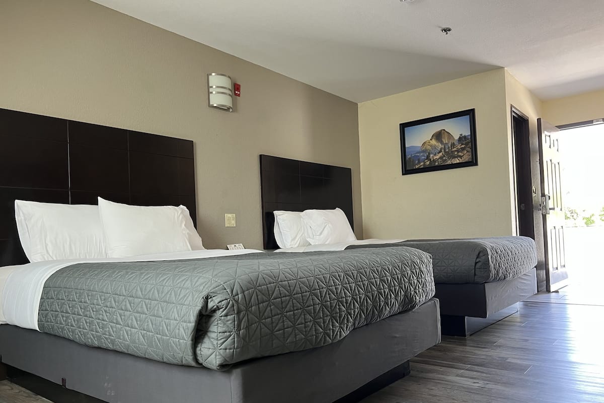 A hotel room with two beds, a painting on the wall, and a door leading outside.