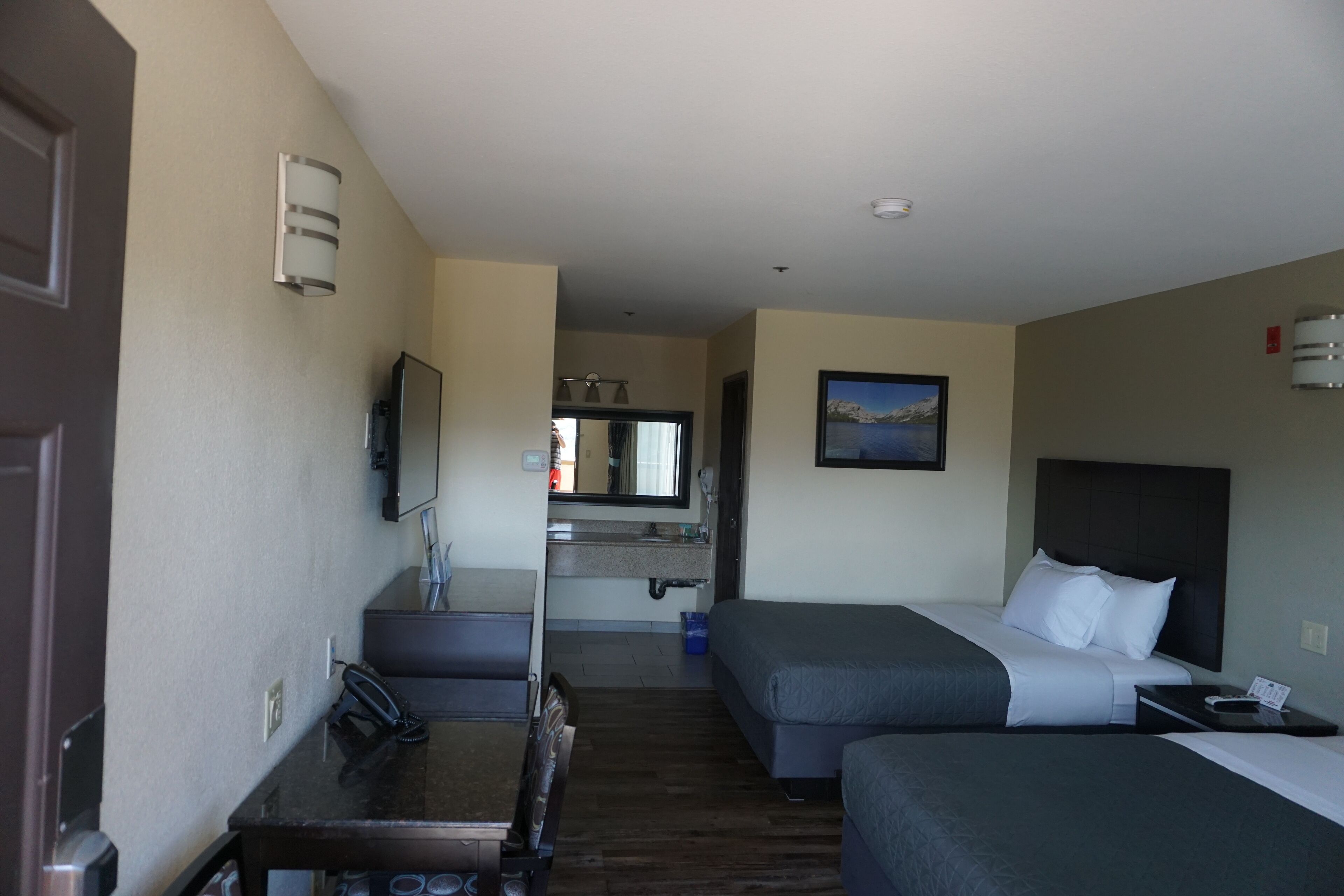 Een hotelkamer met twee bedden, een bureau met telefoon, een televisie en een schilderij aan de muur.