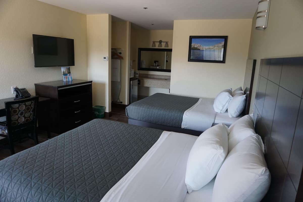 A hotel room with two beds, a desk, a TV, a bathroom, and a view of the mountains.