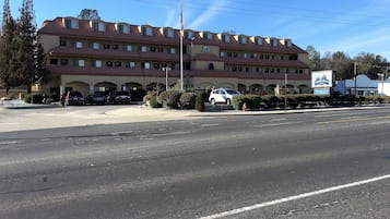 Un hotel de varios pisos con techo rojo y paredes color beige, que cuenta con un estacionamiento con varios autos y una bandera estadounidense visible.