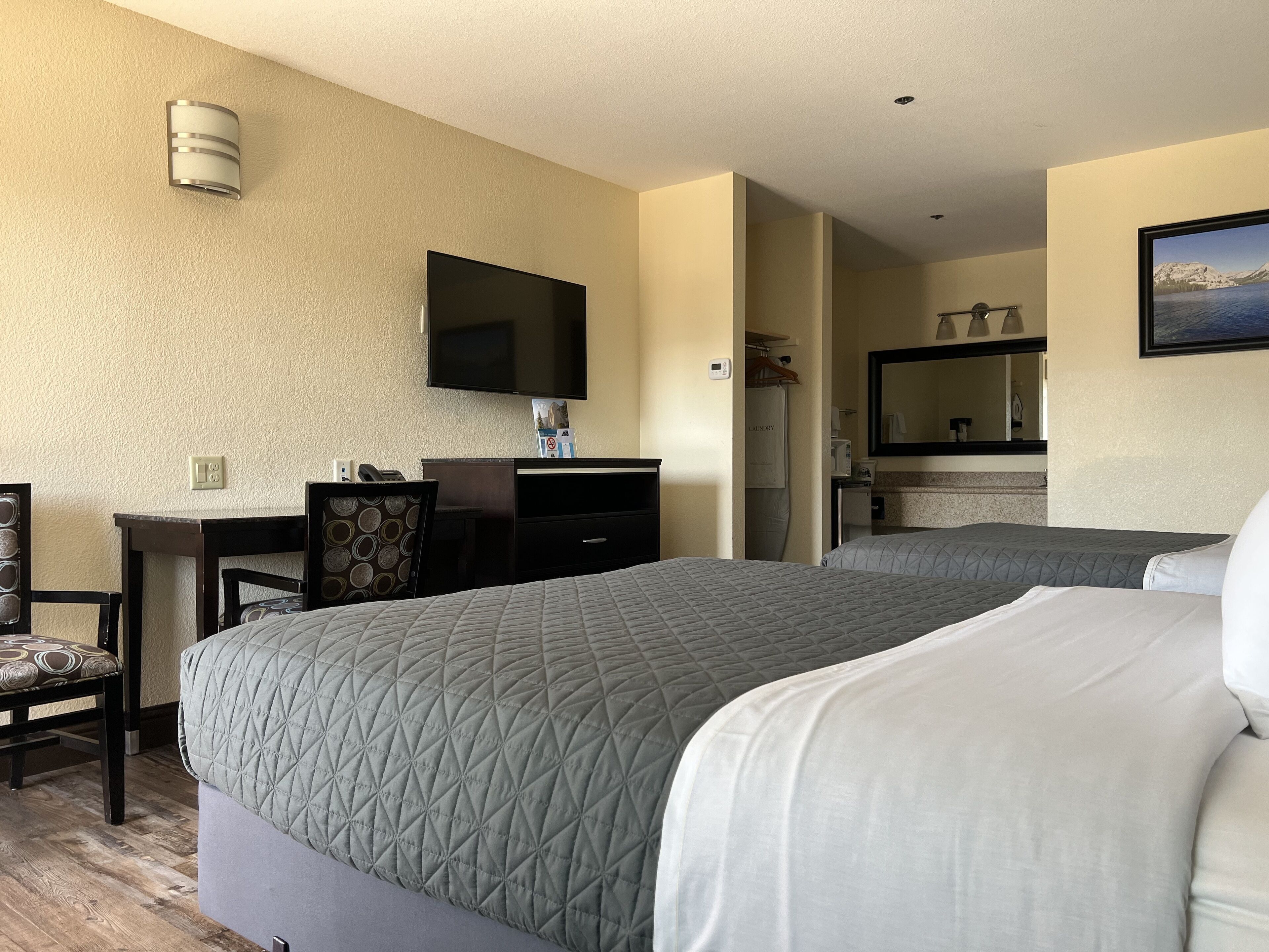 A hotel room with two beds, a desk, a chair, a TV, and a bathroom visible through an open door.