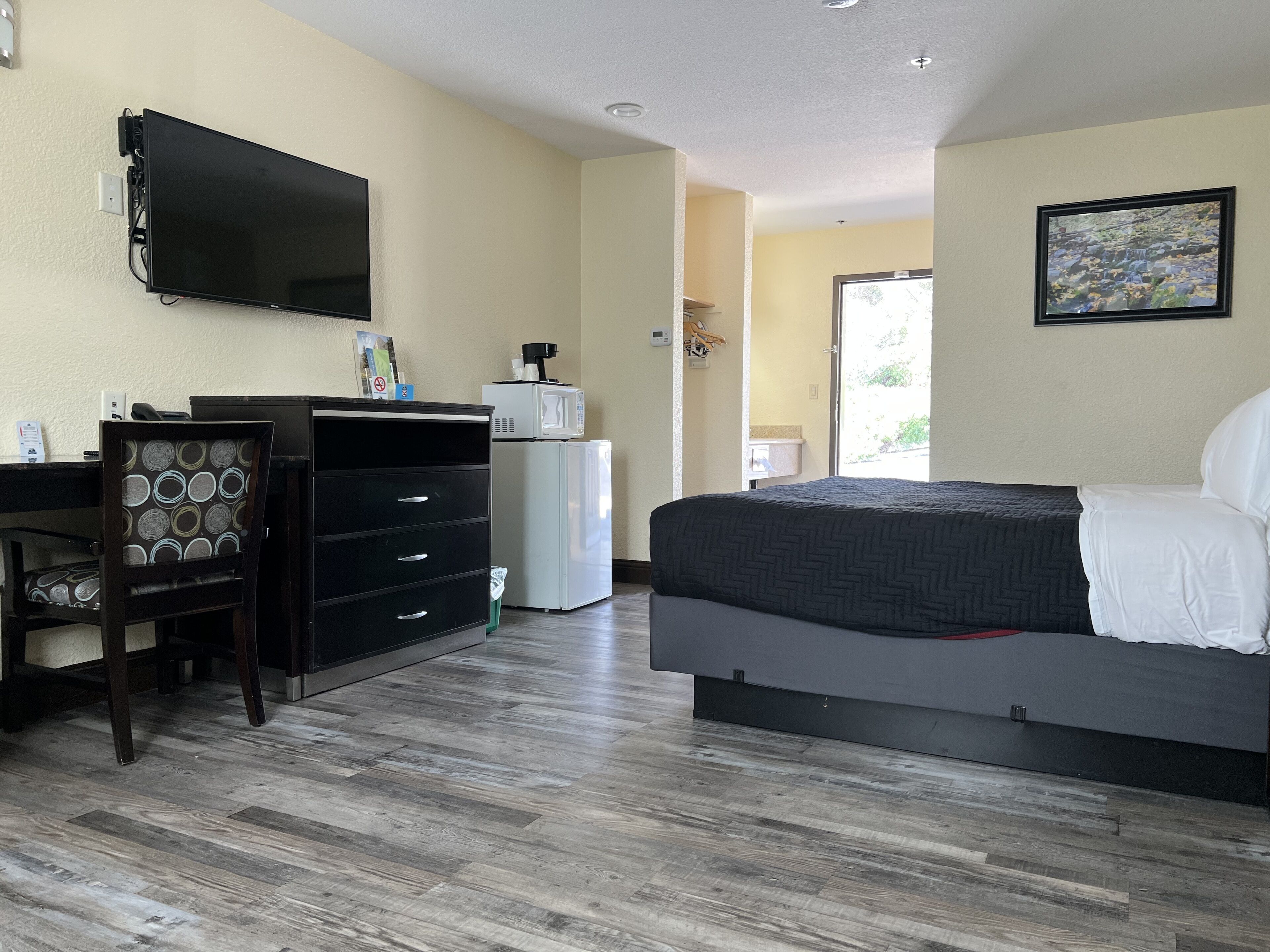 A hotel room with a bed, a desk with a chair, a television, a microwave, and a door leading to a balcony.