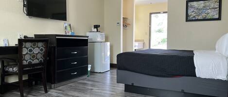 A hotel room with a bed, a desk with a chair, a television, a microwave, and a door leading to a balcony.