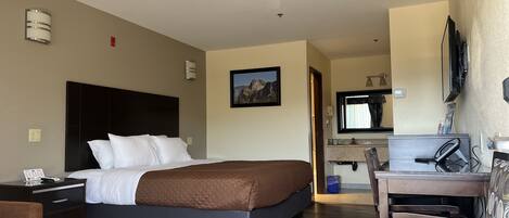 A hotel room with a bed, a desk with a computer, a chair, and a television.