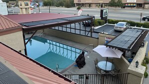 A rooftop pool with a glass enclosure, a covered seating area, and a view of a commercial street with shops.