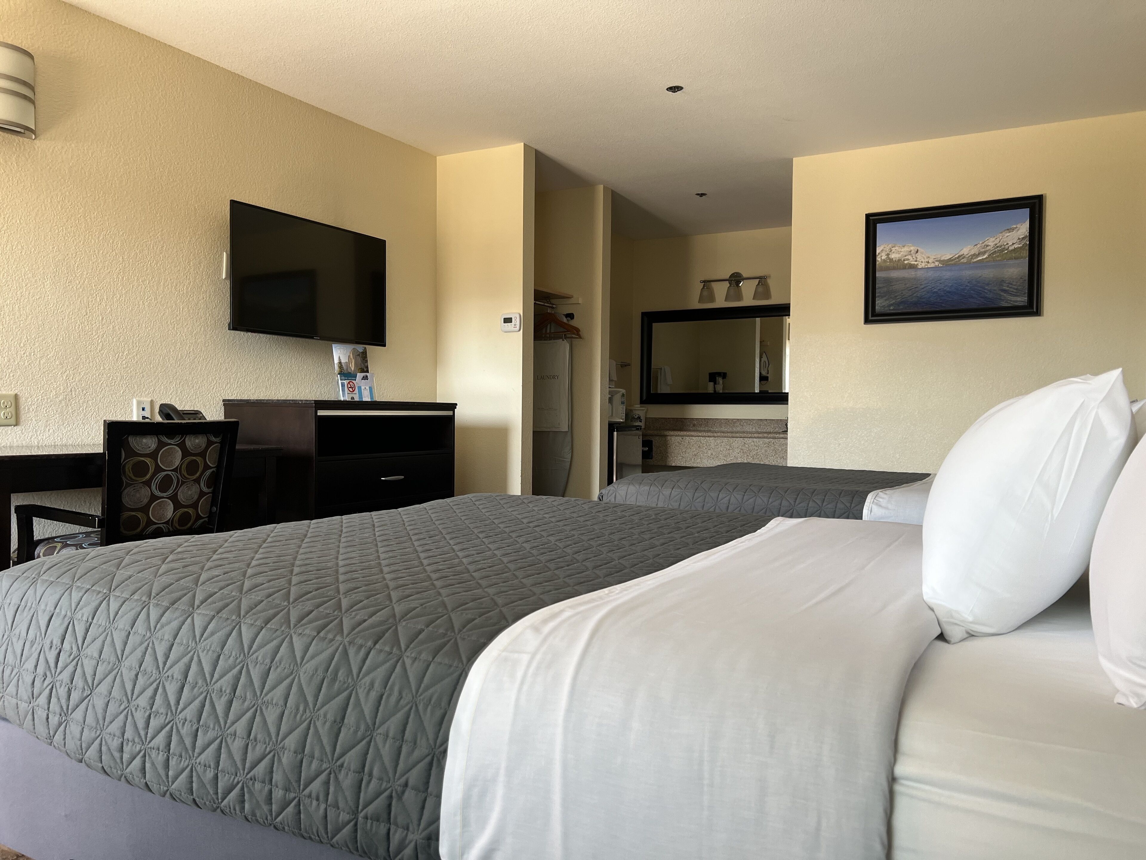 A hotel room with two beds, a desk, a television, a mirror, and a painting.