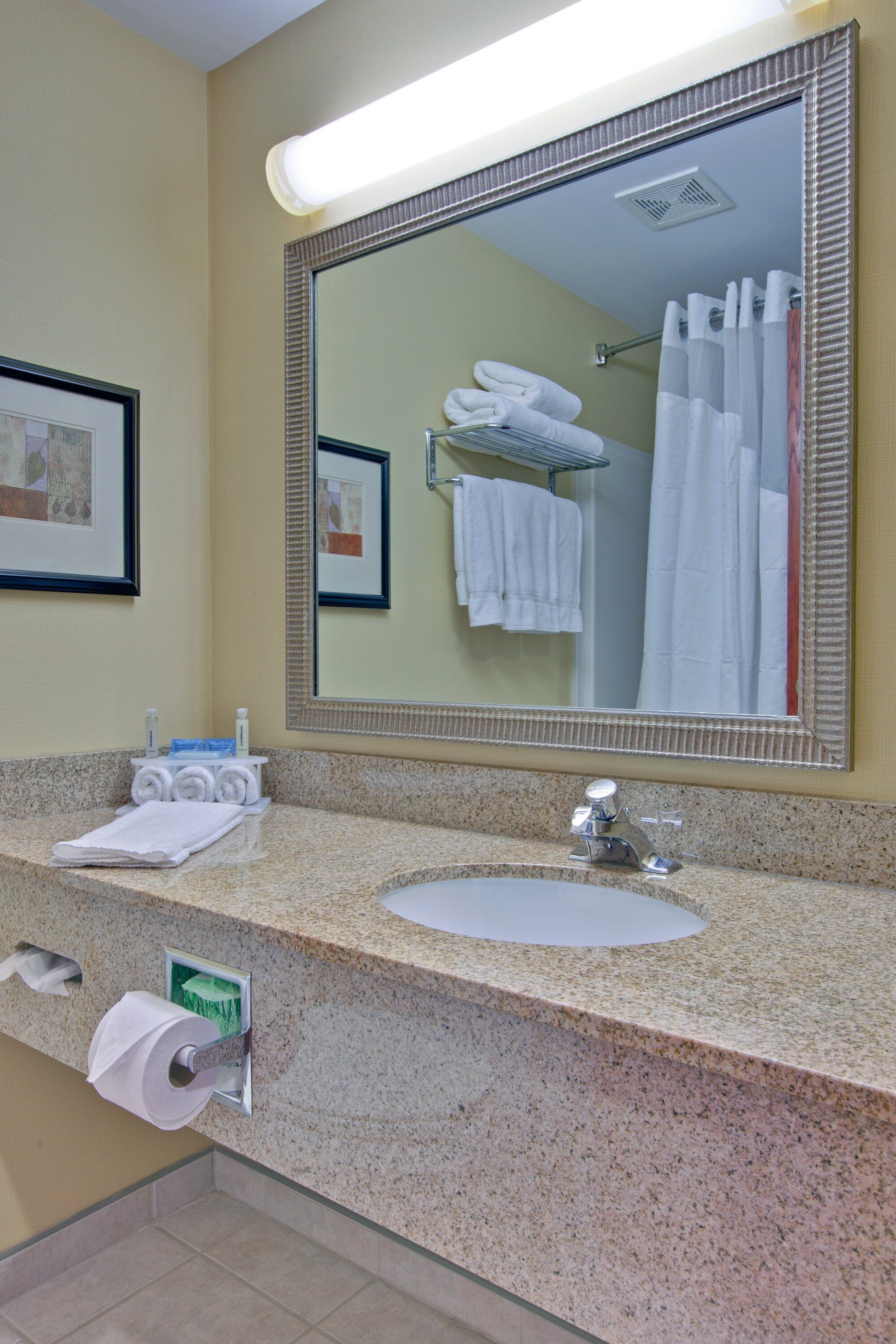 A hotel bathroom with a granite countertop, a sink, a mirror, and a towel rack.