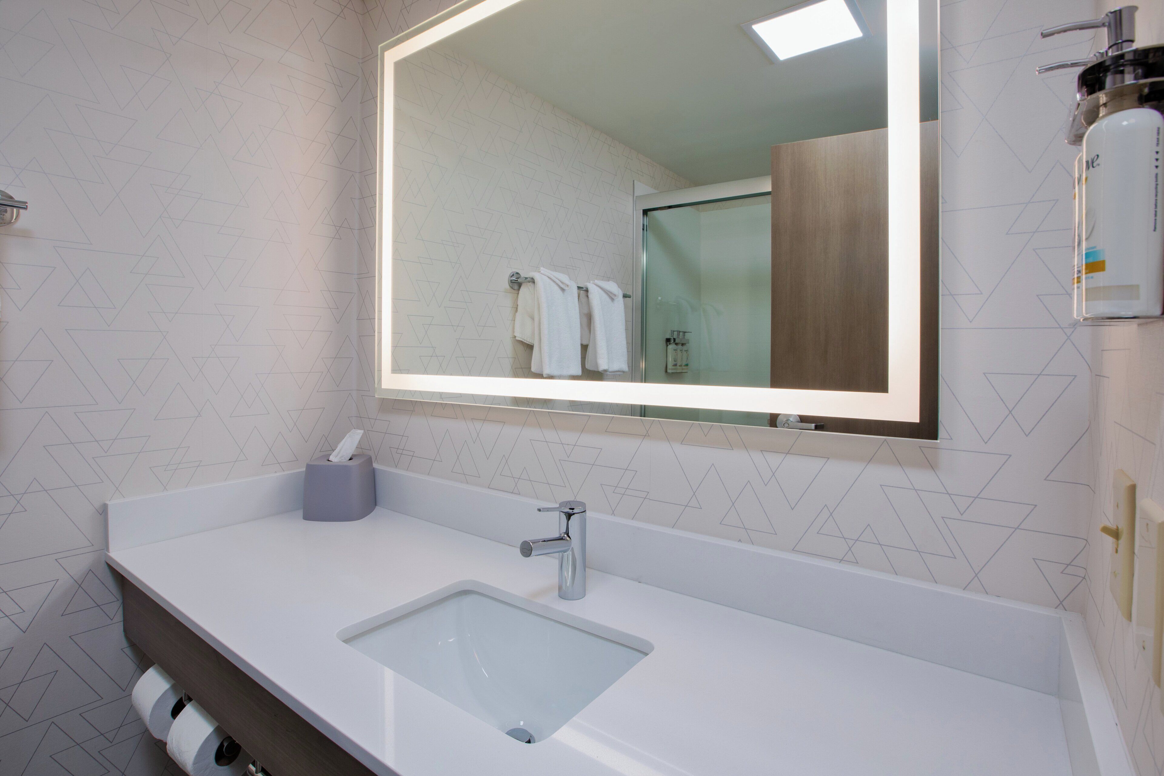 A modern bathroom with a large mirror, a white sink, and a glass-enclosed shower.