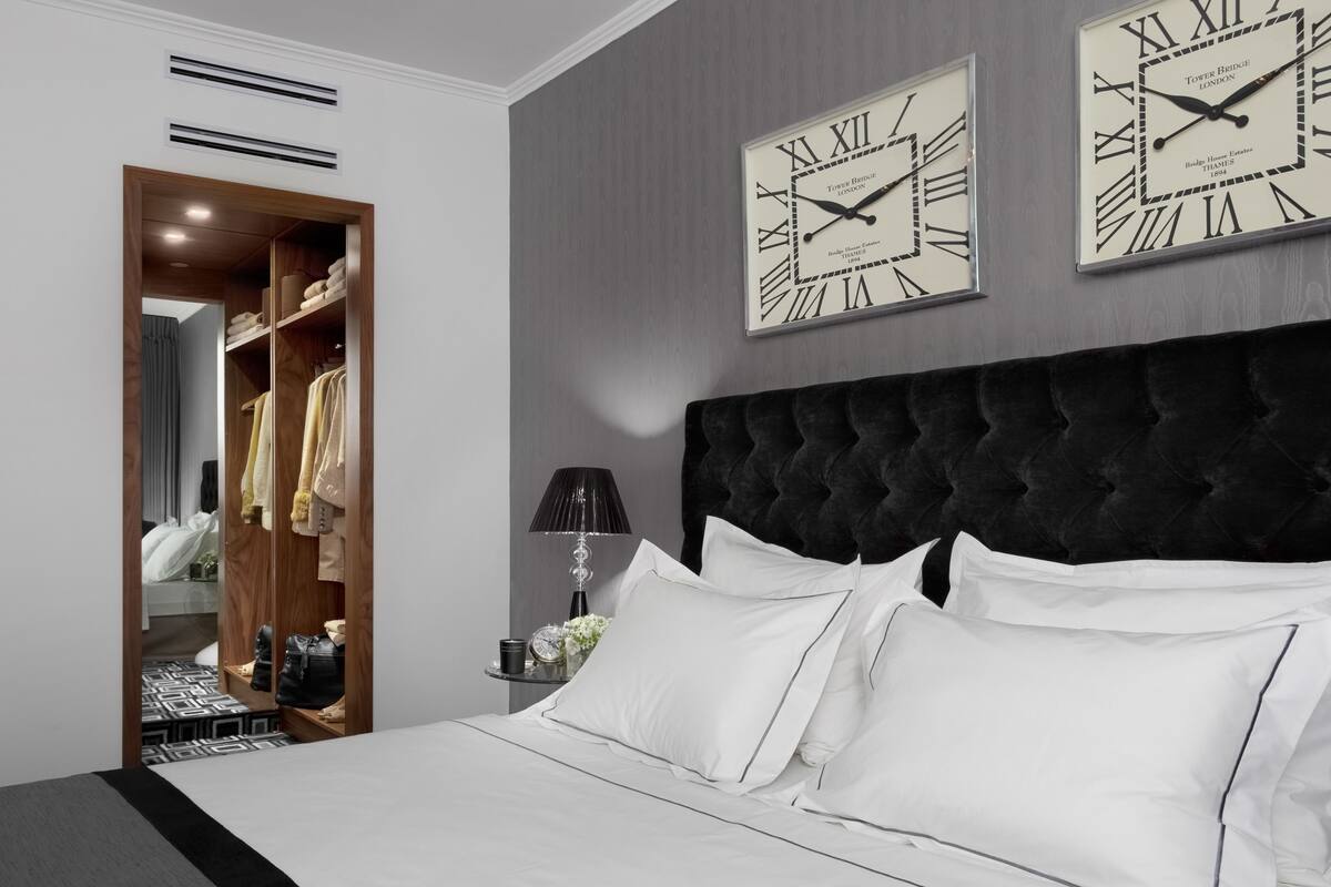 Een slaapkamer met een groot bed, een donker hoofdeinde en twee wandklokken.