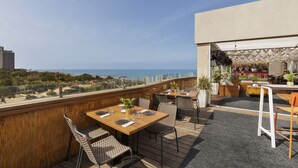 Une terrasse sur le toit, avec des tables et des chaises, un espace bar et une vue sur l’océan.
