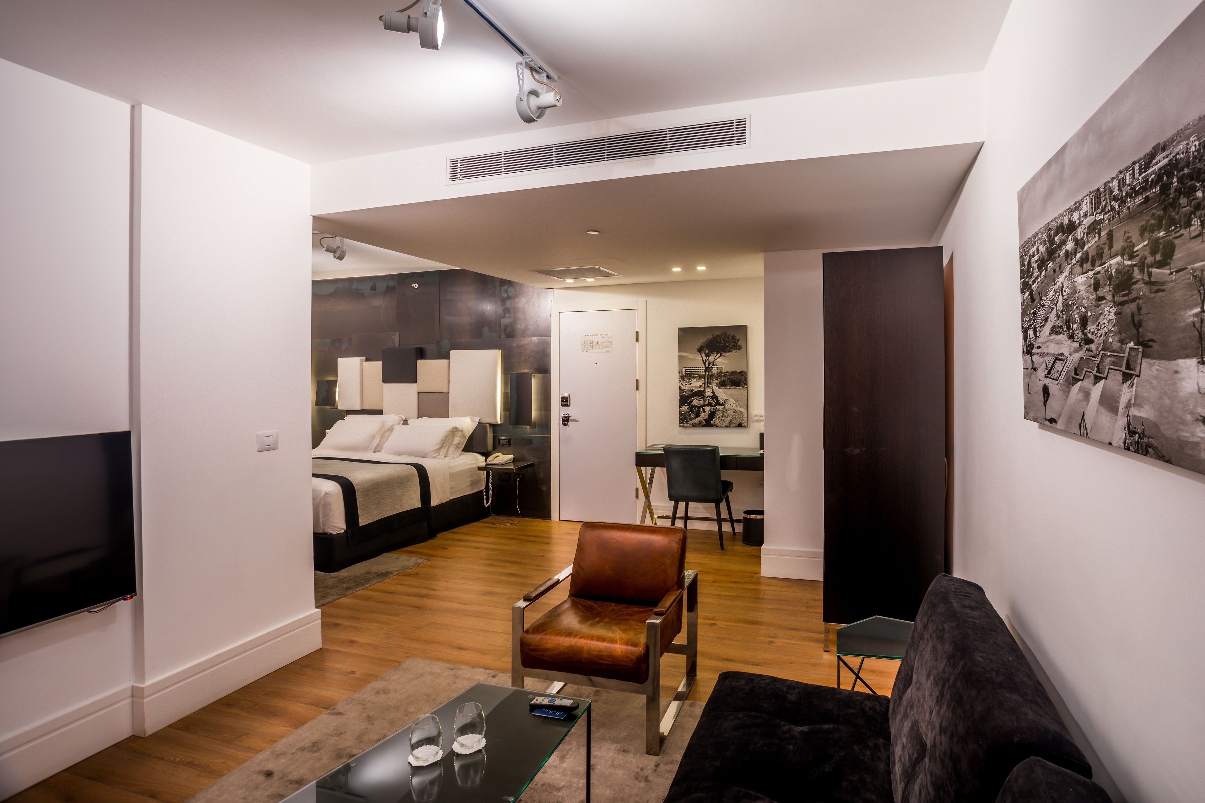 Una habitación de hotel moderna con una cama, un escritorio, una silla, un televisor y un cuadro grande en la pared.