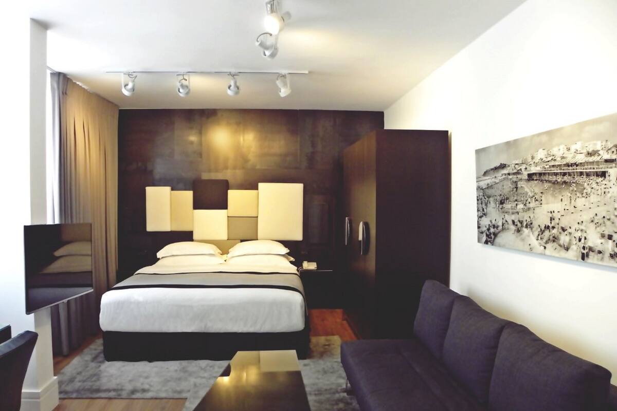 Een moderne hotelkamer met een groot bed, een donkere bank, een klein tafeltje en een tv aan de muur.