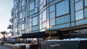 Un hôtel moderne avec une façade en verre, un espace extérieur aménagé pour s’asseoir et une enseigne.