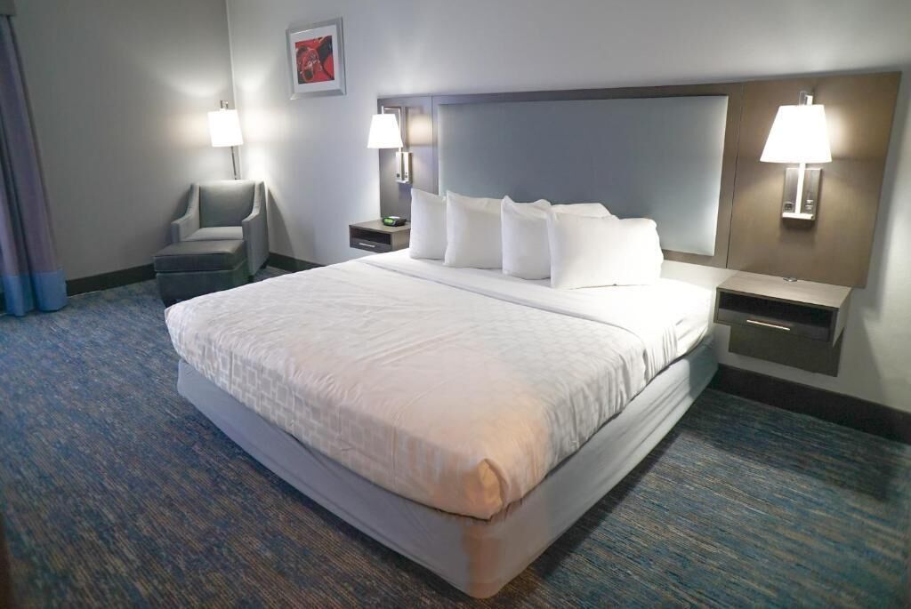 A hotel room with a large bed, two bedside tables with lamps, a chair, and a carpeted floor.