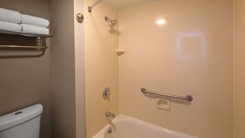 Un baño con bañera, ducha e inodoro. Hay toallas en un estante y un asidero en la ducha.