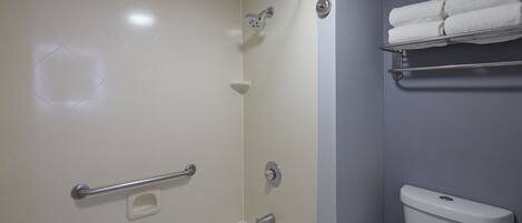 A bathroom with a shower, grab bar, toilet, and towel rack.