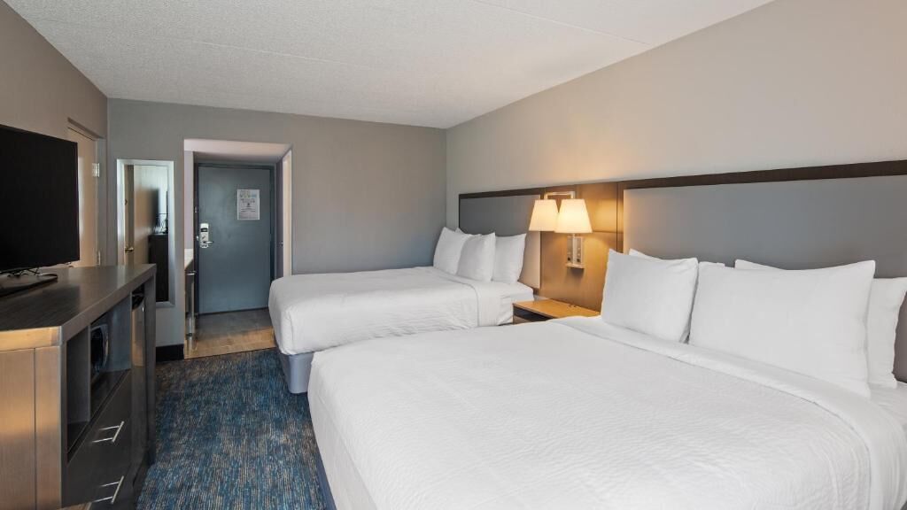 Habitación de hotel con dos camas, televisión, escritorio y lámpara.