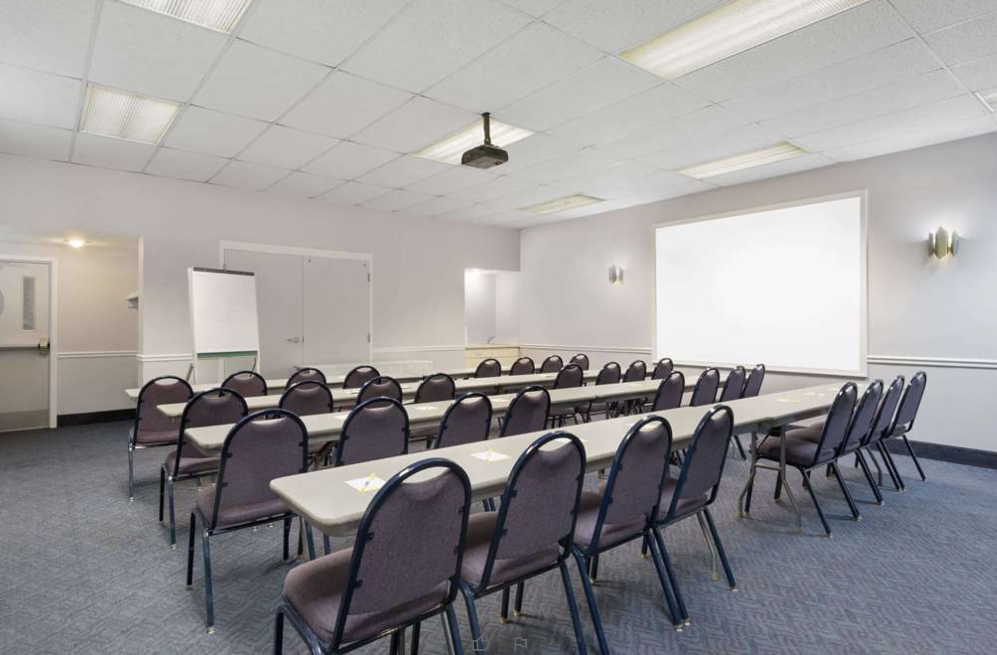 A conference room with a long table, chairs, a projector screen, and a whiteboard.
