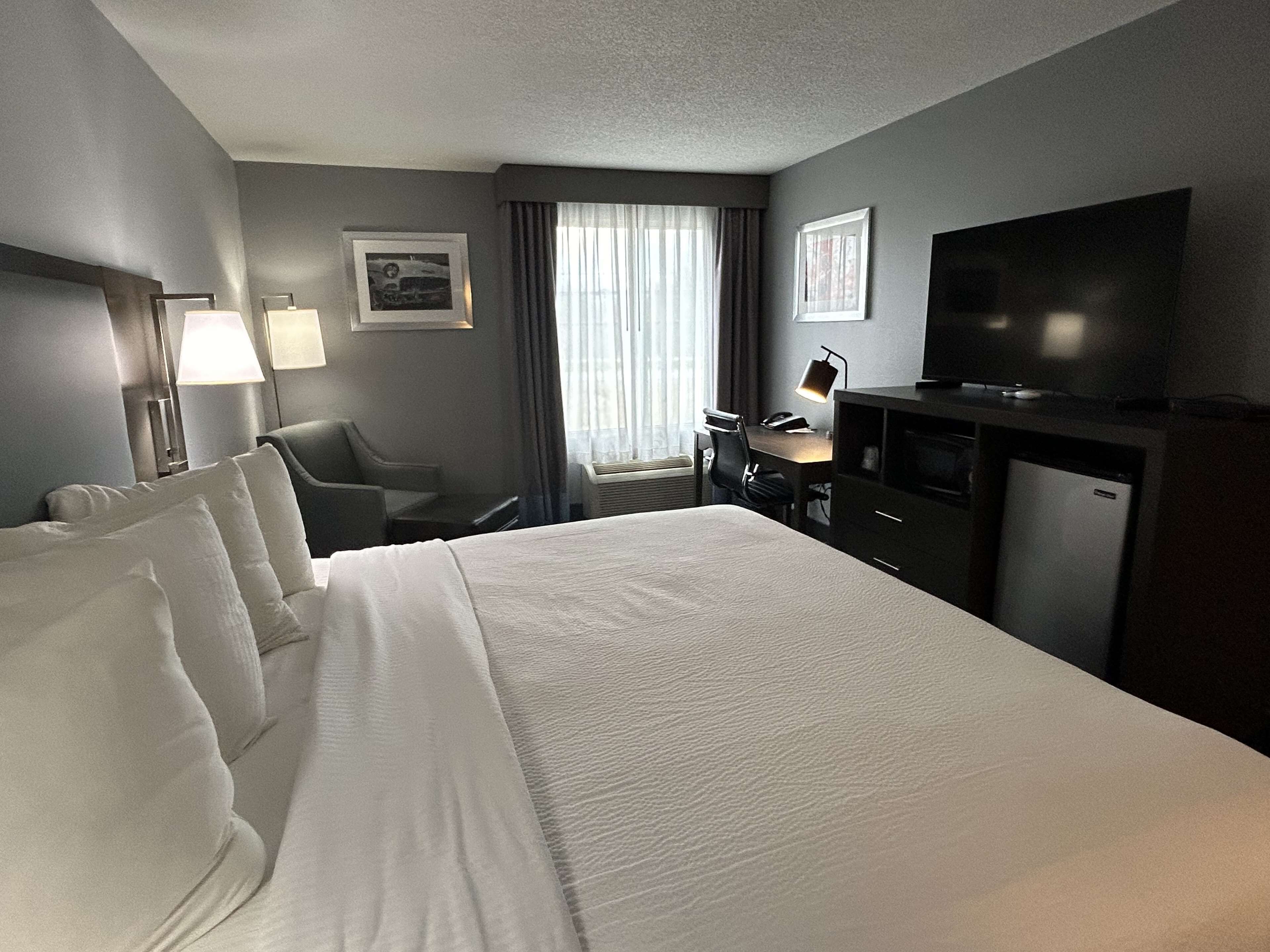 Habitación de hotel con una cama grande, un escritorio con silla, un televisor y una ventana con cortinas.