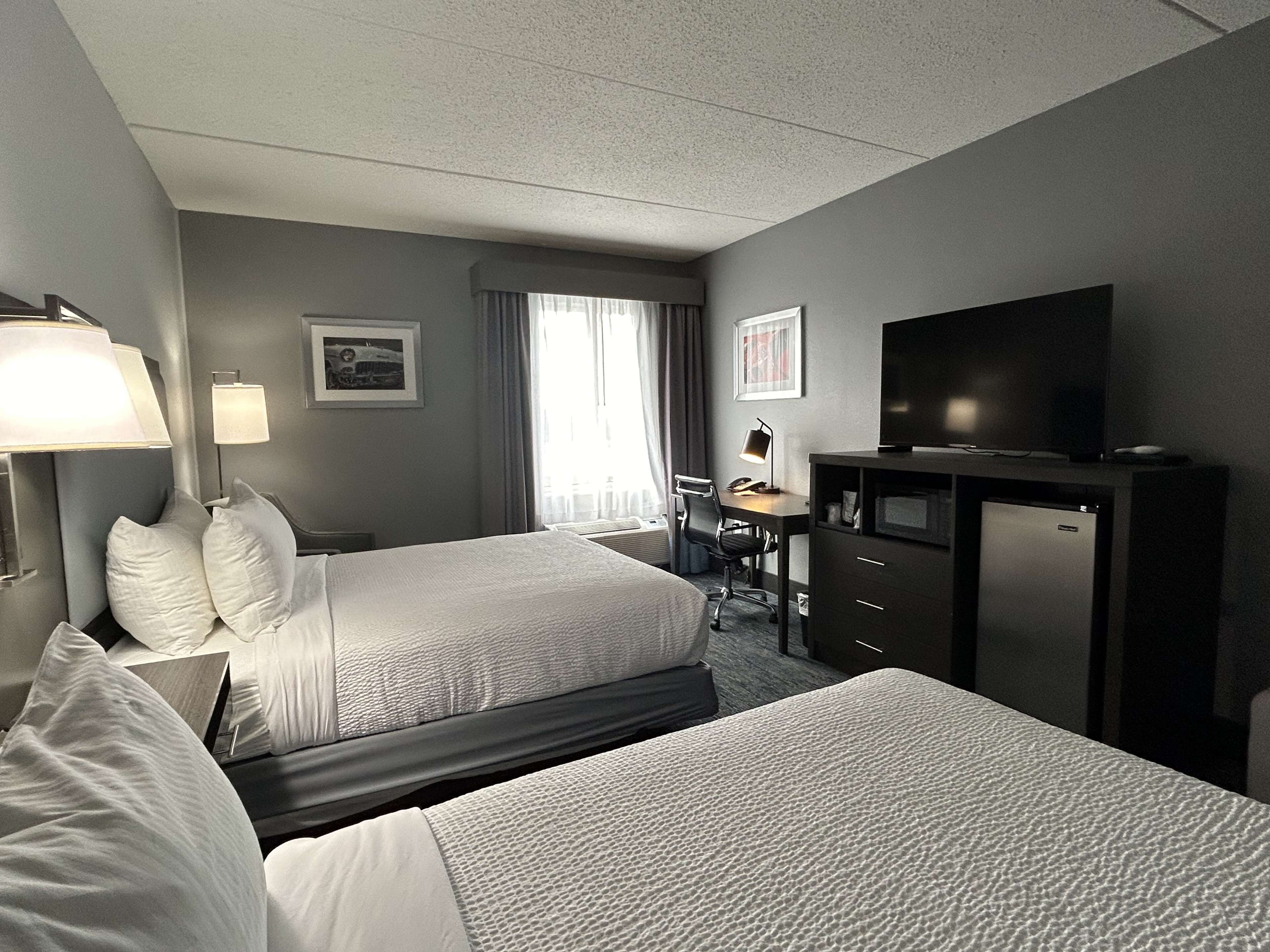 A hotel room with two beds, a desk, a television, and a desk lamp.