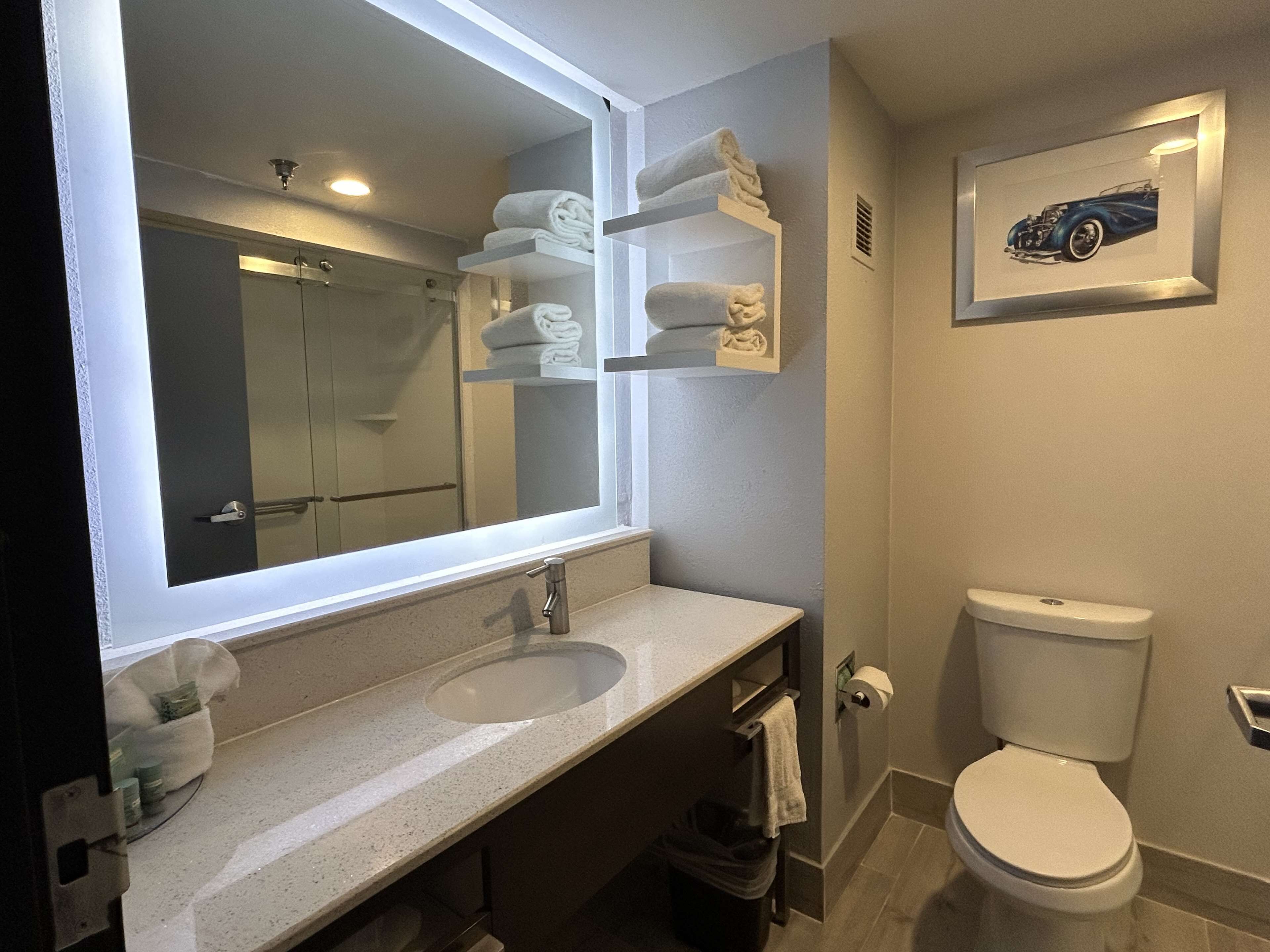 Une salle de bain avec un grand miroir, deux lavabos, des toilettes et un porte-serviettes avec des serviettes pliées.
