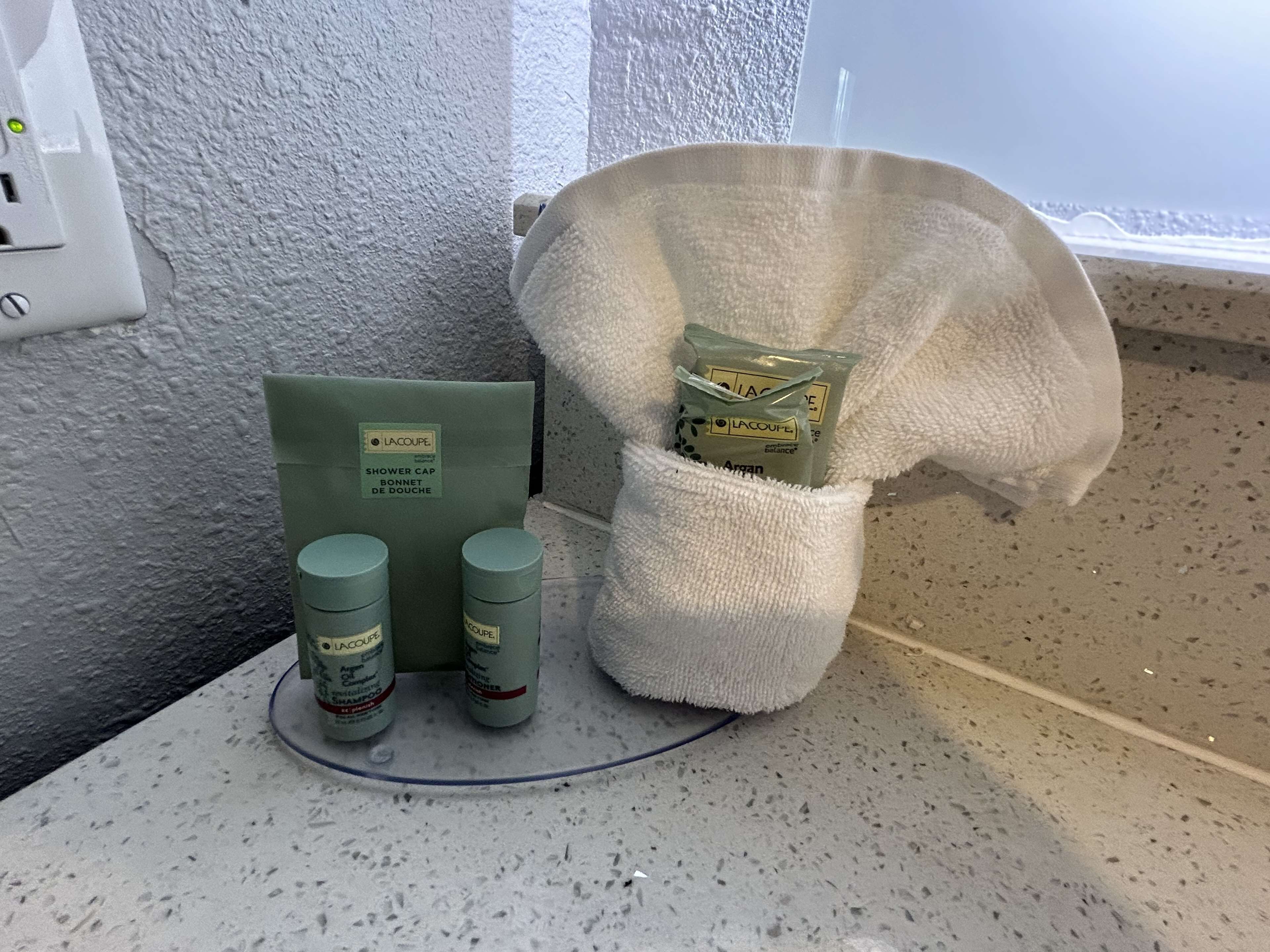 Et badeværelsesbord med en brusebadshætte, shampoo og et håndklæde.