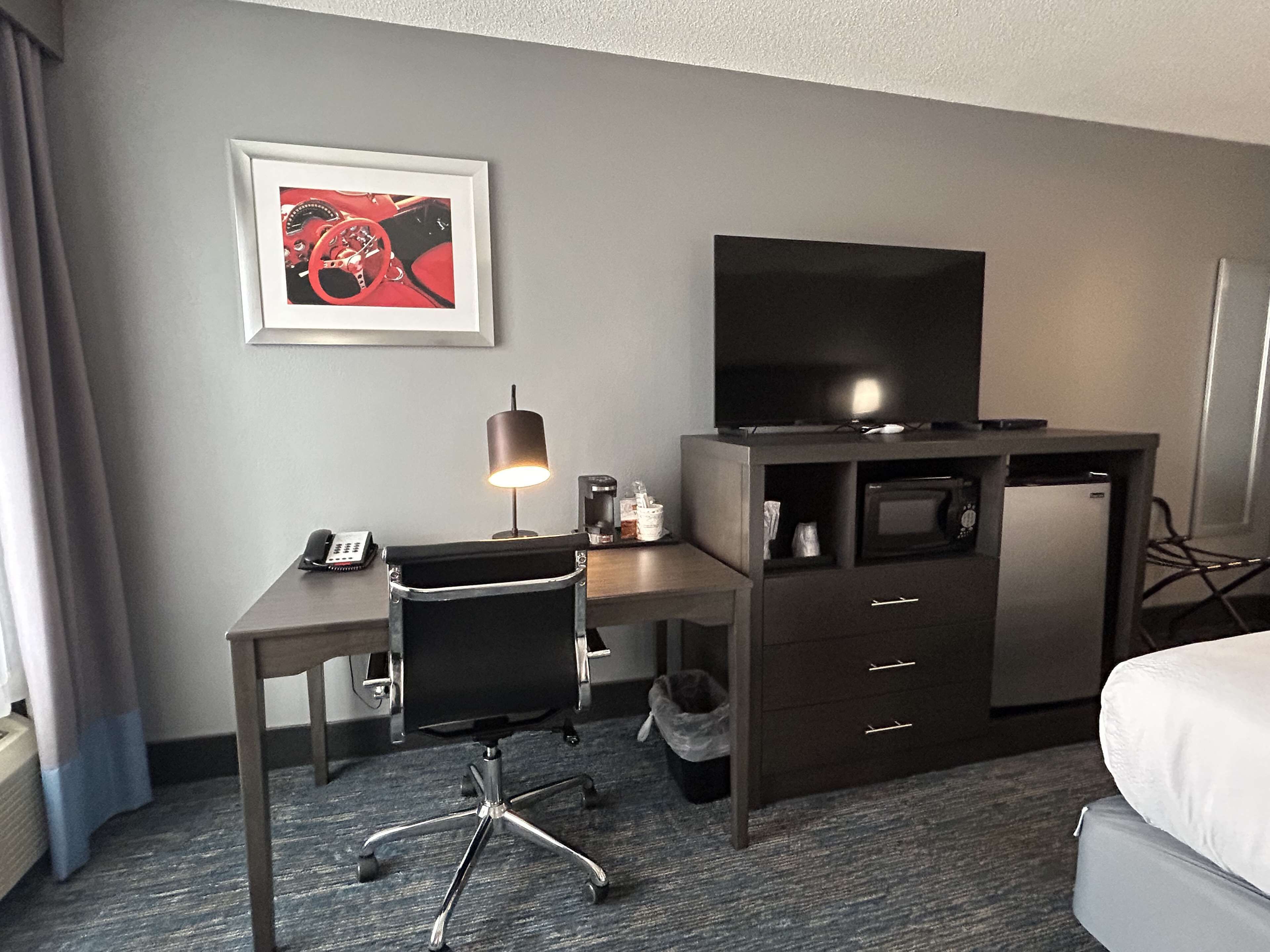 A hotel room with a desk, chair, television, and a bed.