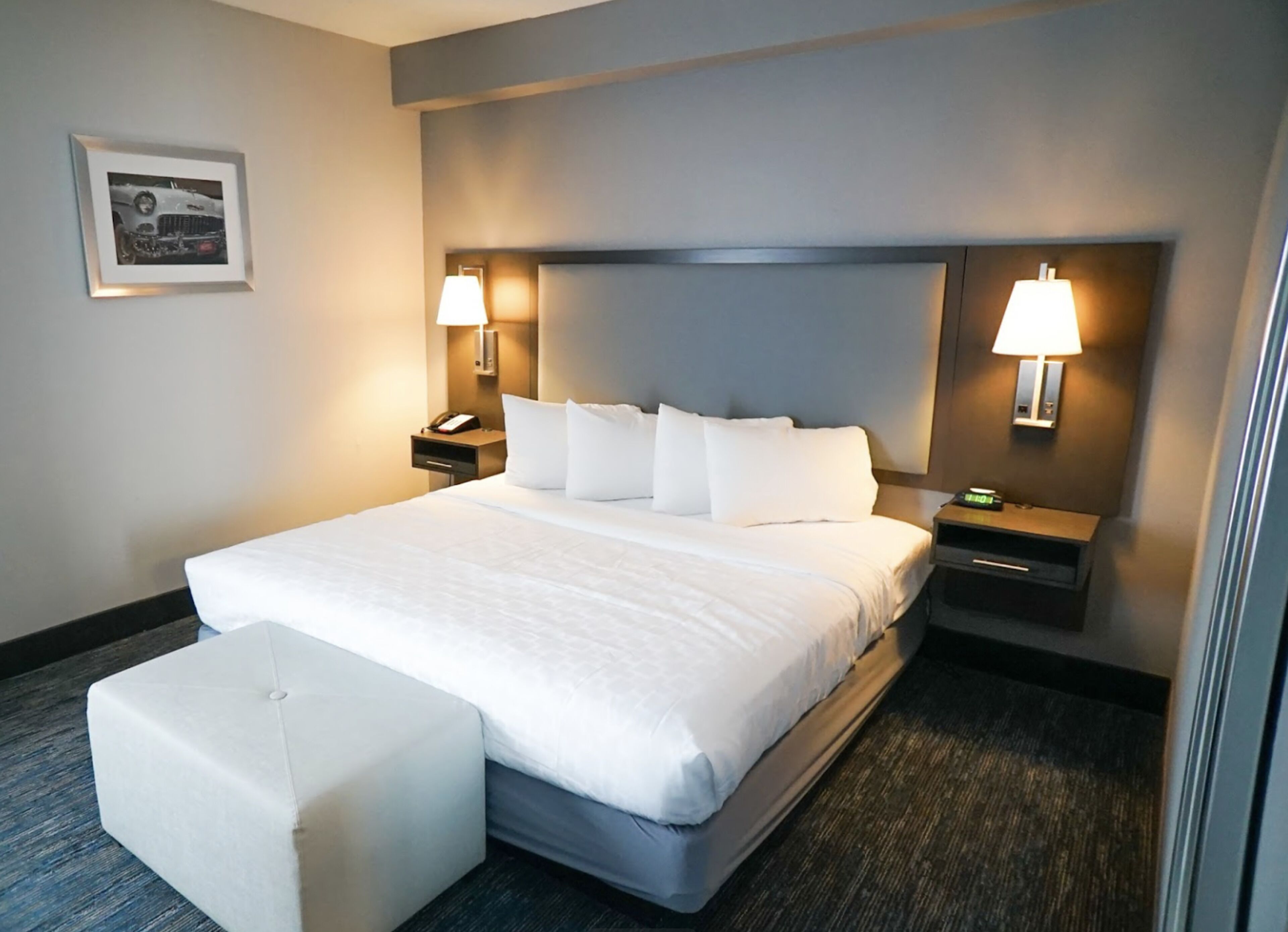 Hotelkamer met een groot bed, twee nachtkastjes met lampen, een bijzettafeltje, een ingelijste foto aan de muur en een vloerbedekking.