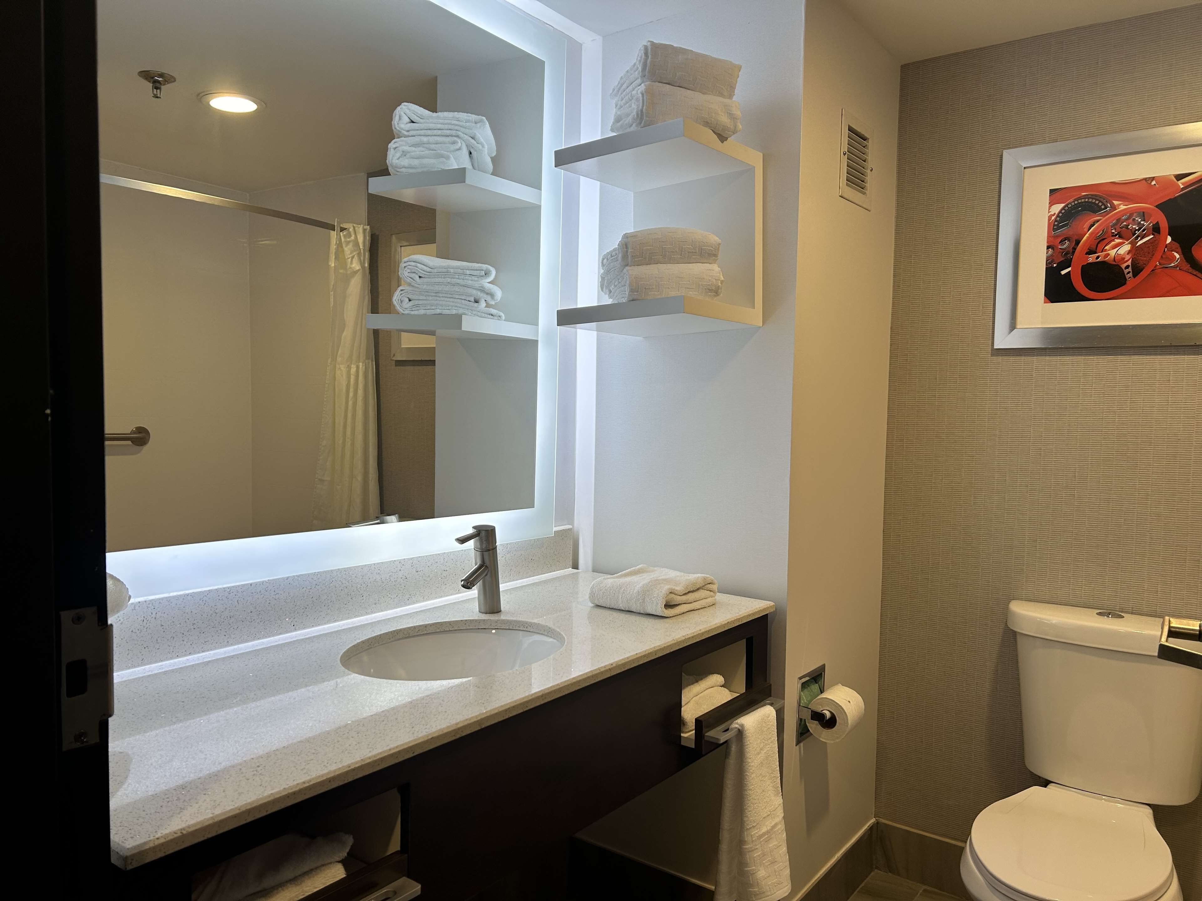 A modern bathroom with a large mirror, a sink, a toilet, and towel storage.