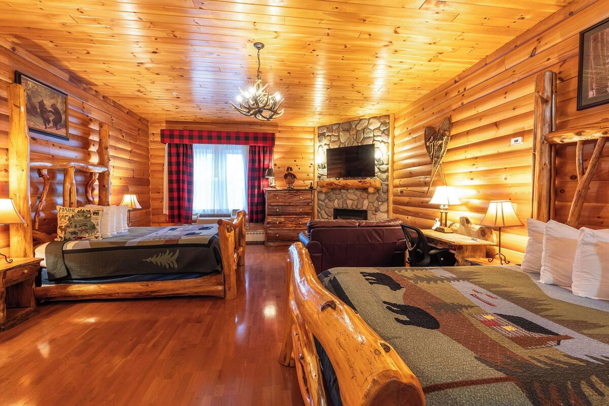 A log cabin-style room with two beds, a fireplace, a television, and wooden walls.