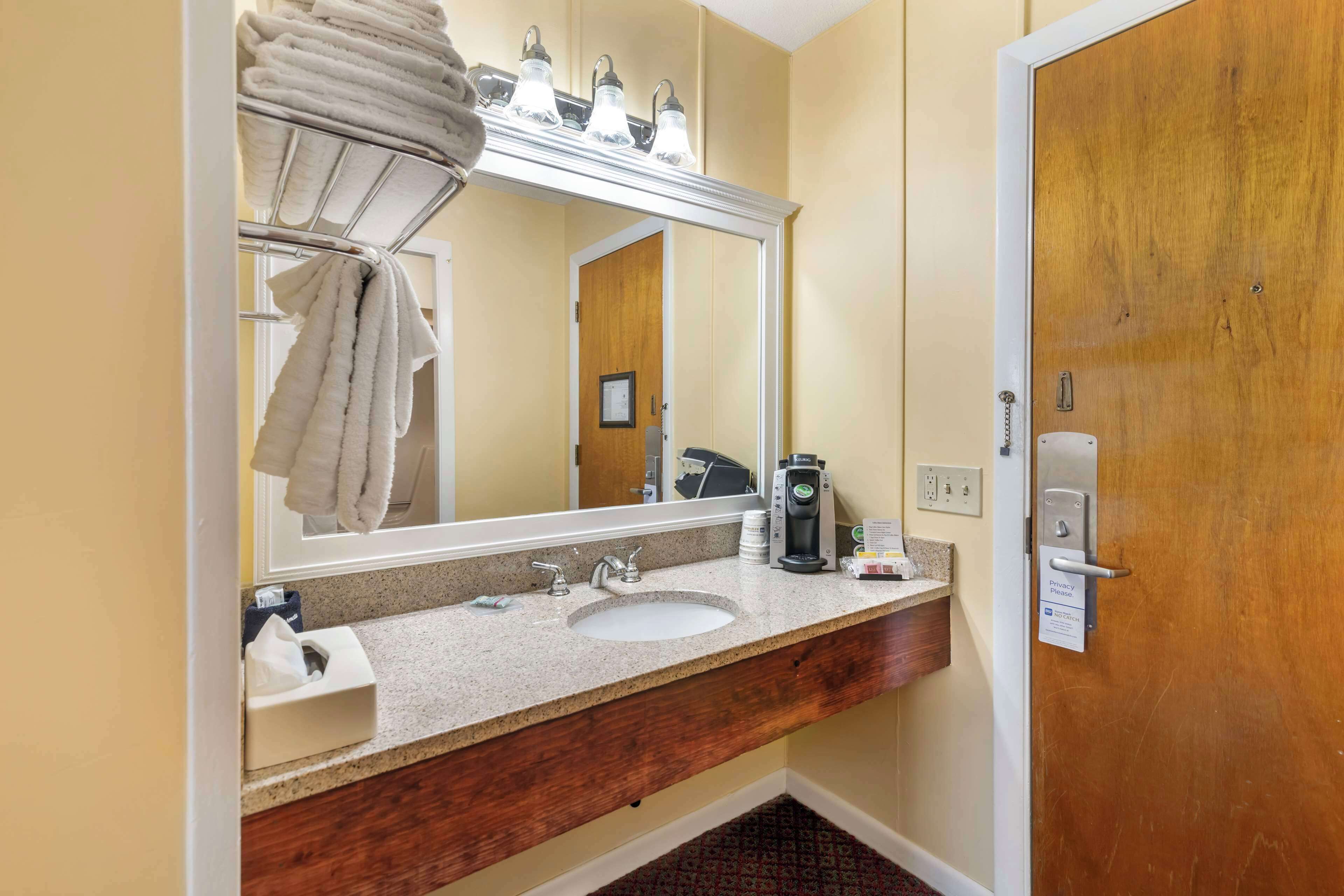 Un baño de hotel con lavamanos, espejo, perchero para toallas y cartel de privacidad.