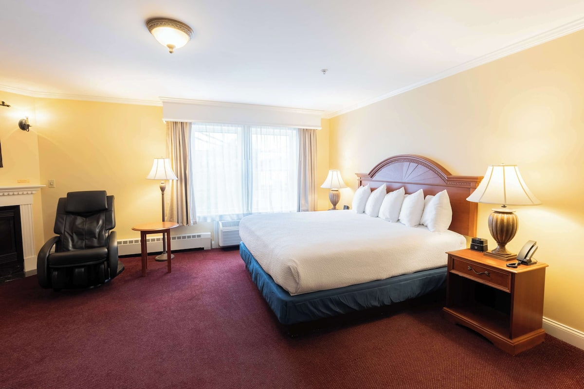 A hotel room with a large bed, a massage chair, a small table, and a nightstand with a lamp.