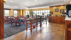 A spacious dining area with wooden tables and chairs, a buffet setup, and large windows providing natural light.
