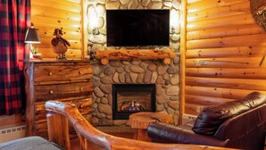 A log cabin interior with a stone fireplace, a leather sofa, and a mounted television.