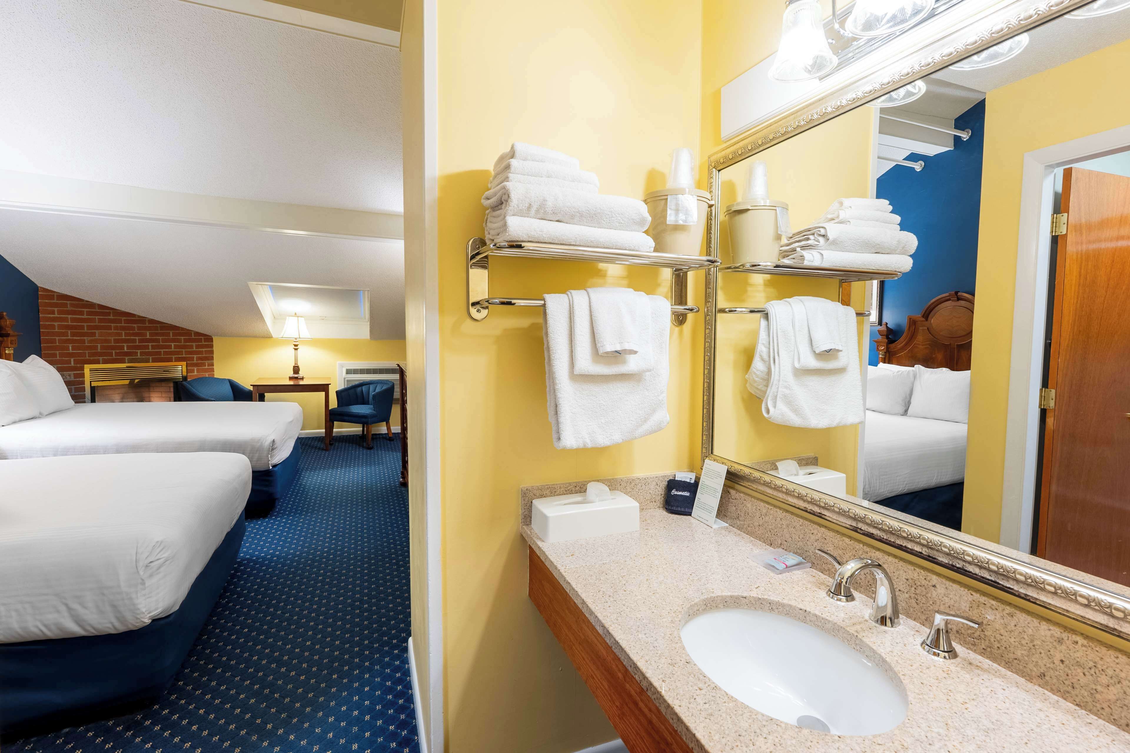 Hotellihuone, jossa on kaksi sänkyä, kylpyhuone, jossa on pesuallas, peili ja pyyheteline.