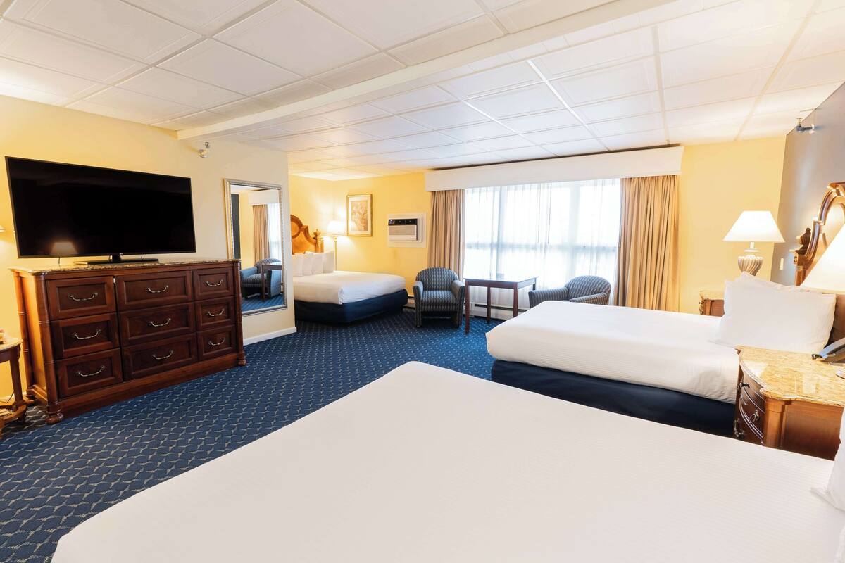 A hotel room with a large bed, a smaller bed, a flat-screen TV, a dresser, a chair, and a desk with a lamp.