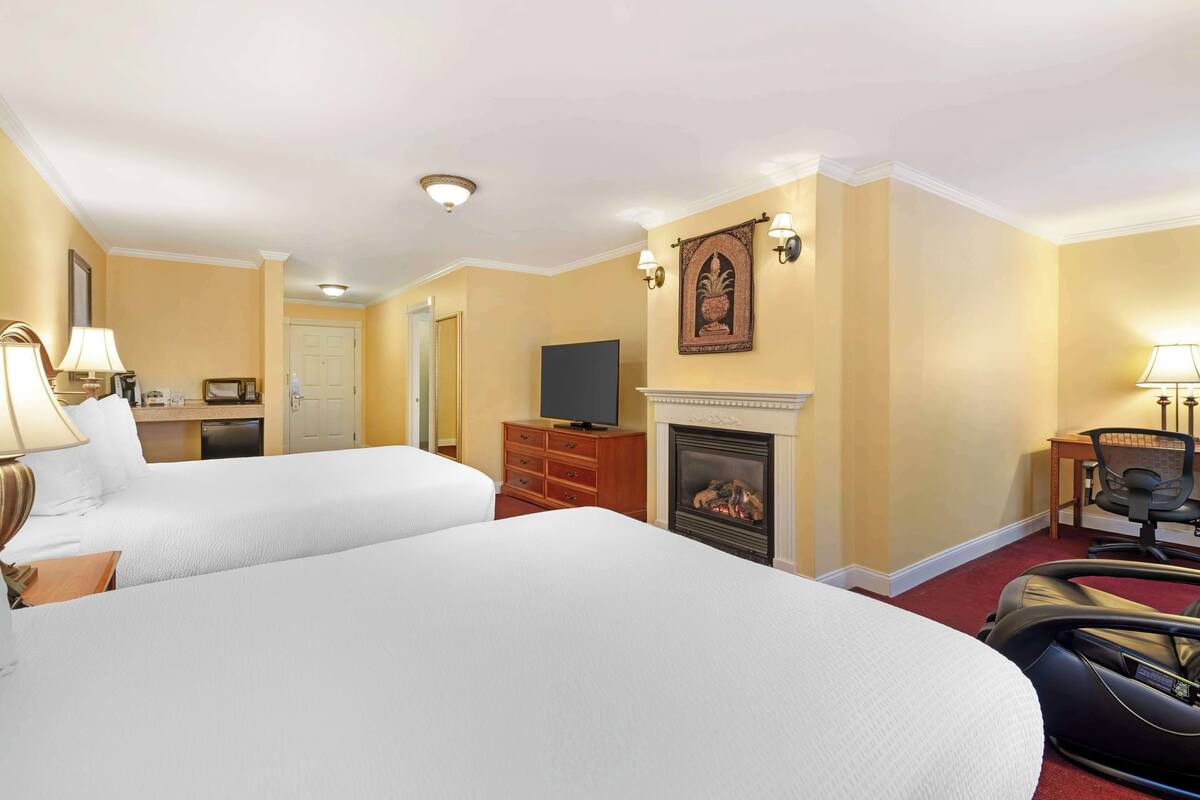 A hotel room with two beds, a fireplace, a television, and a desk with a lamp.