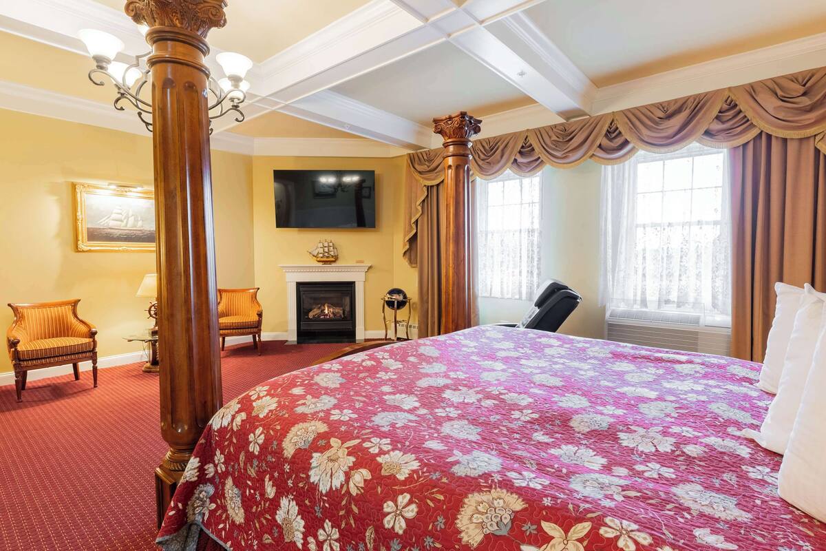 A hotel room with a large bed, a fireplace, a television, and two chairs.