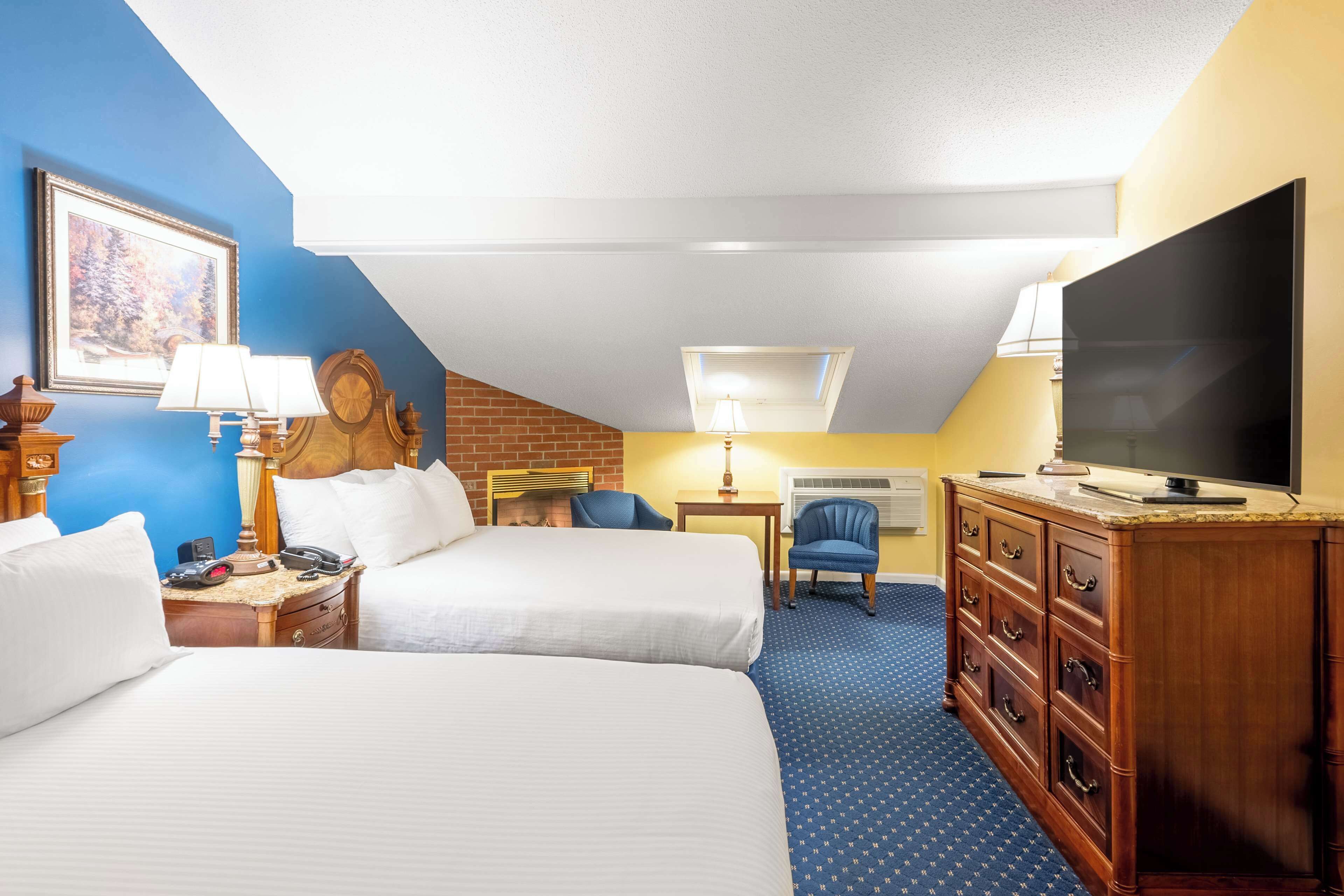 A hotel room with two beds, a TV, a desk with a lamp, a chair, and a dresser.
