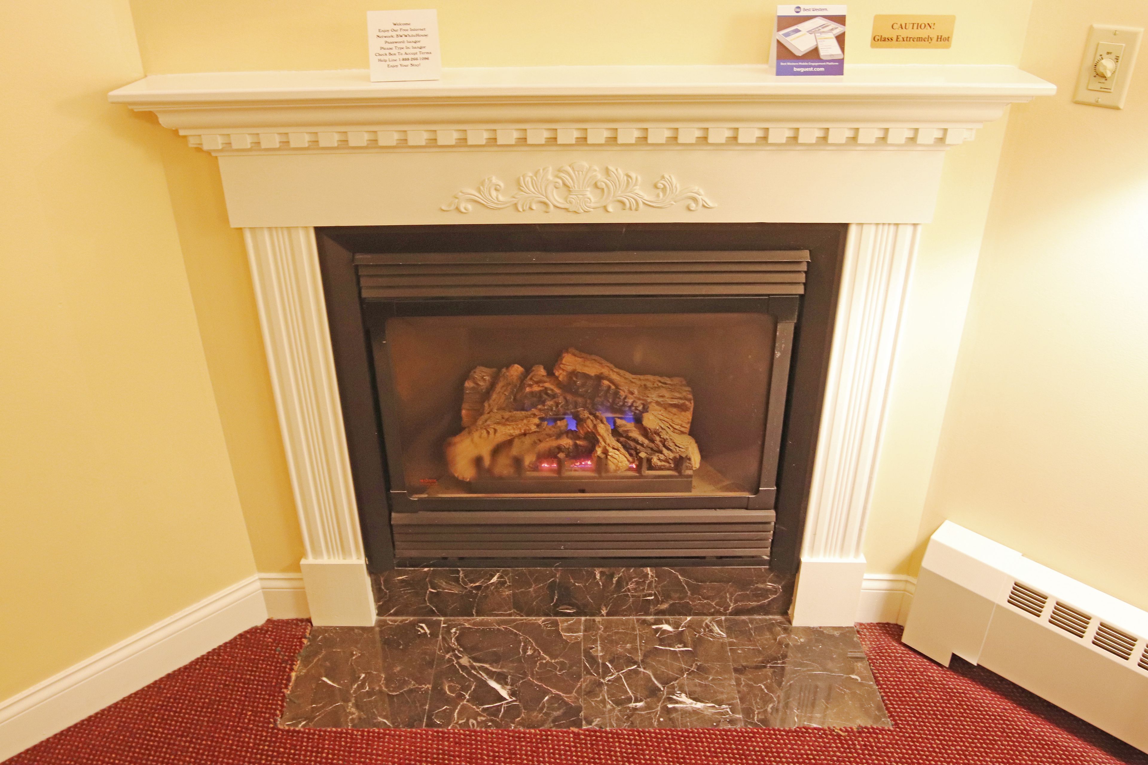 A fireplace with a marble surround, a white mantel, and a red carpeted floor.