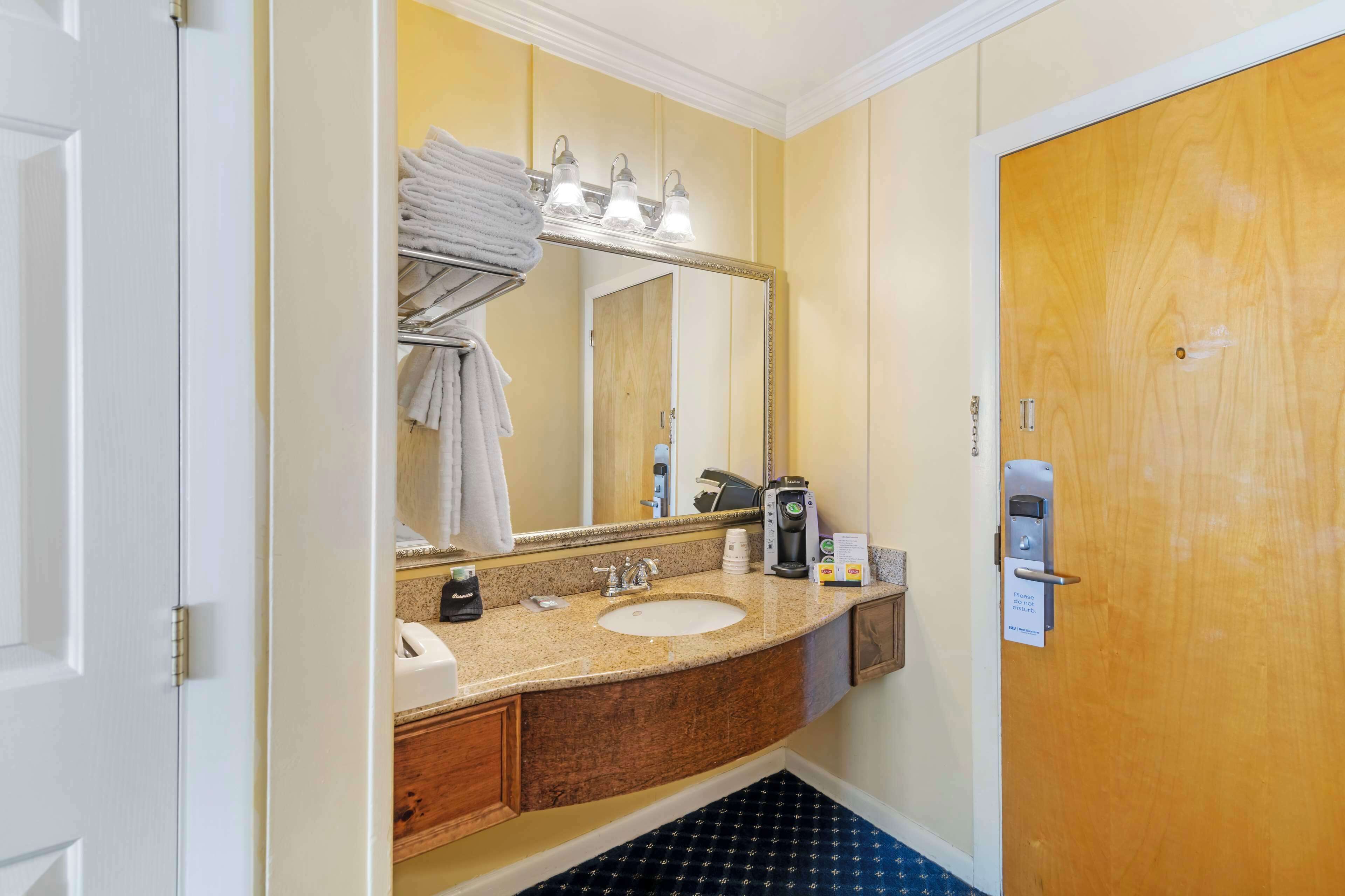 A bathroom with a sink, mirror, towel rack, and a door with a lock.
