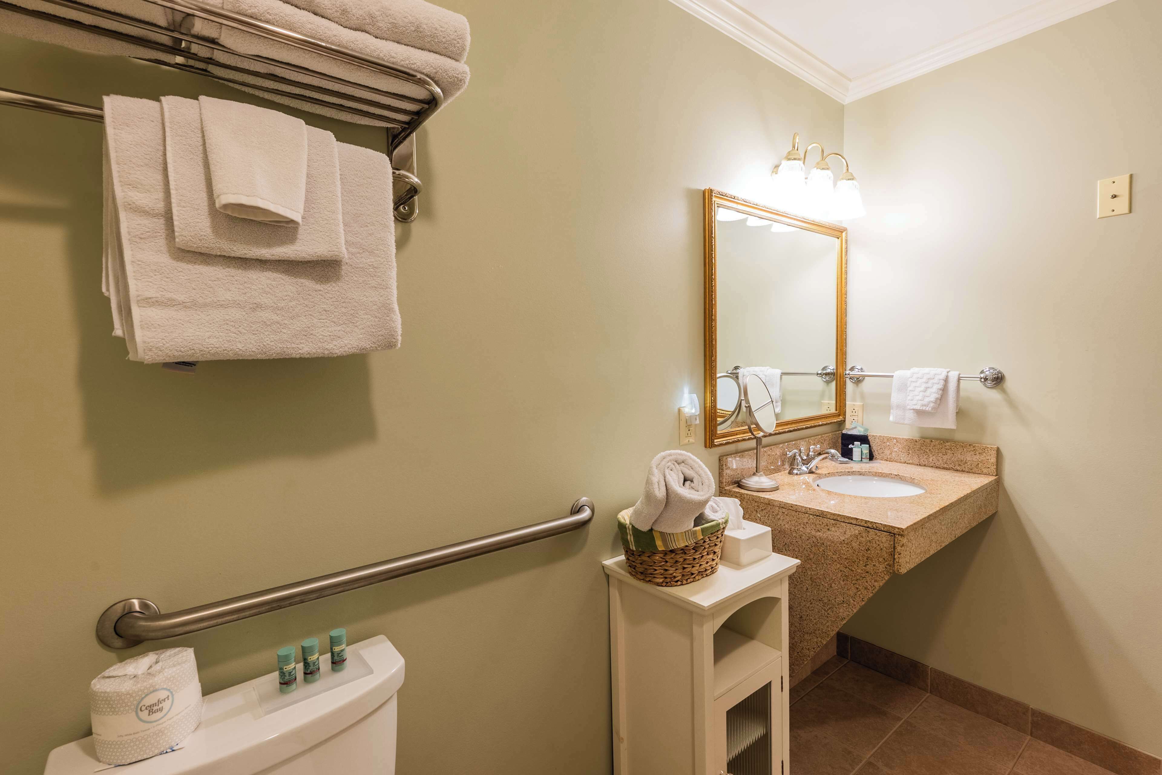 Een badkamer met toilet, wastafel en spiegel. Handdoeken hangen aan de muur en er staat een mand met handdoeken op de wastafel.