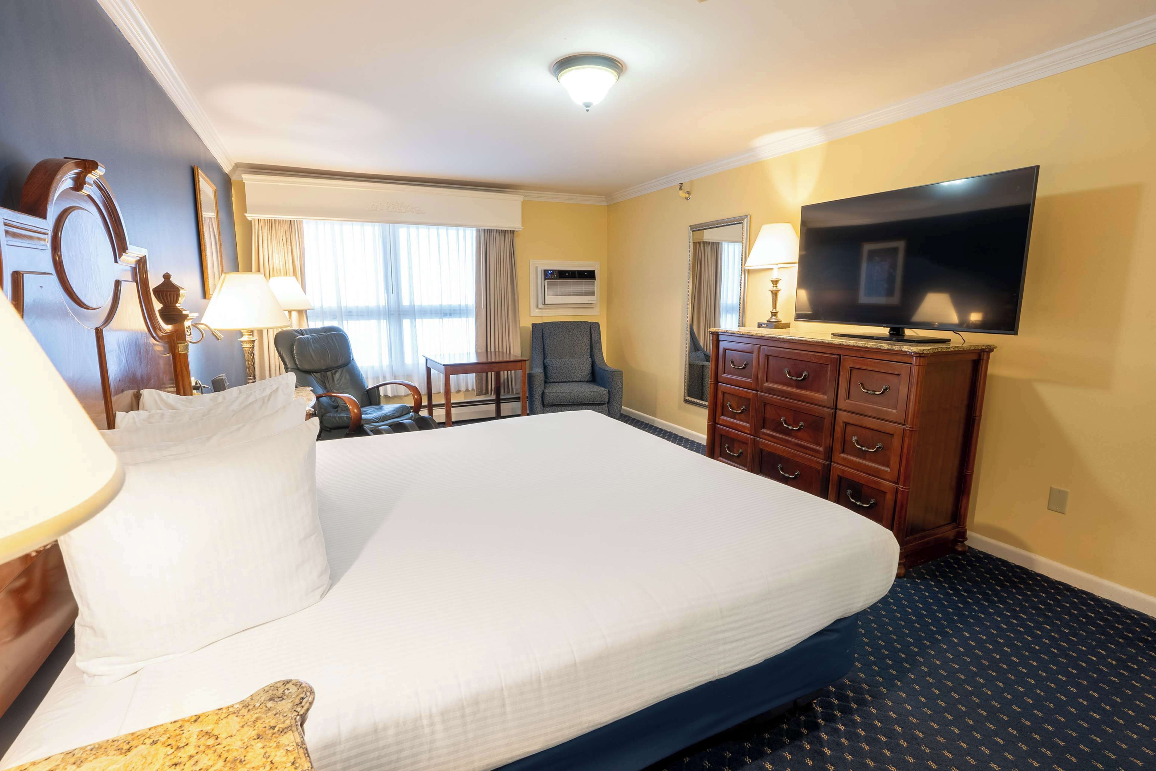 Hotelkamer met een groot bed, een flatscreen televisie, een bureau met stoel, een kast en een raam met gordijnen.