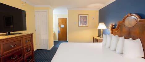 A hotel room with a large bed, a TV, a wooden dresser, and a nightstand with a lamp.