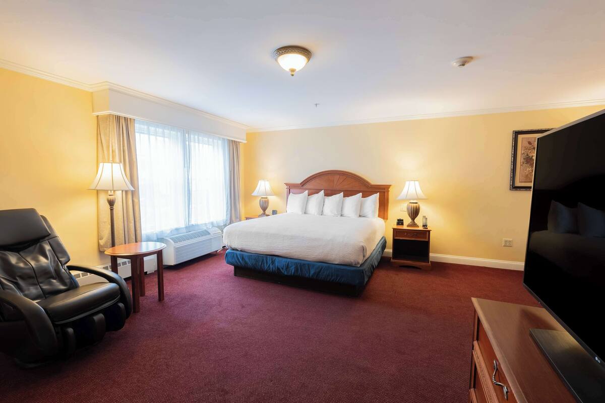 A hotel room with a bed, a massage chair, a TV, and a window with curtains.