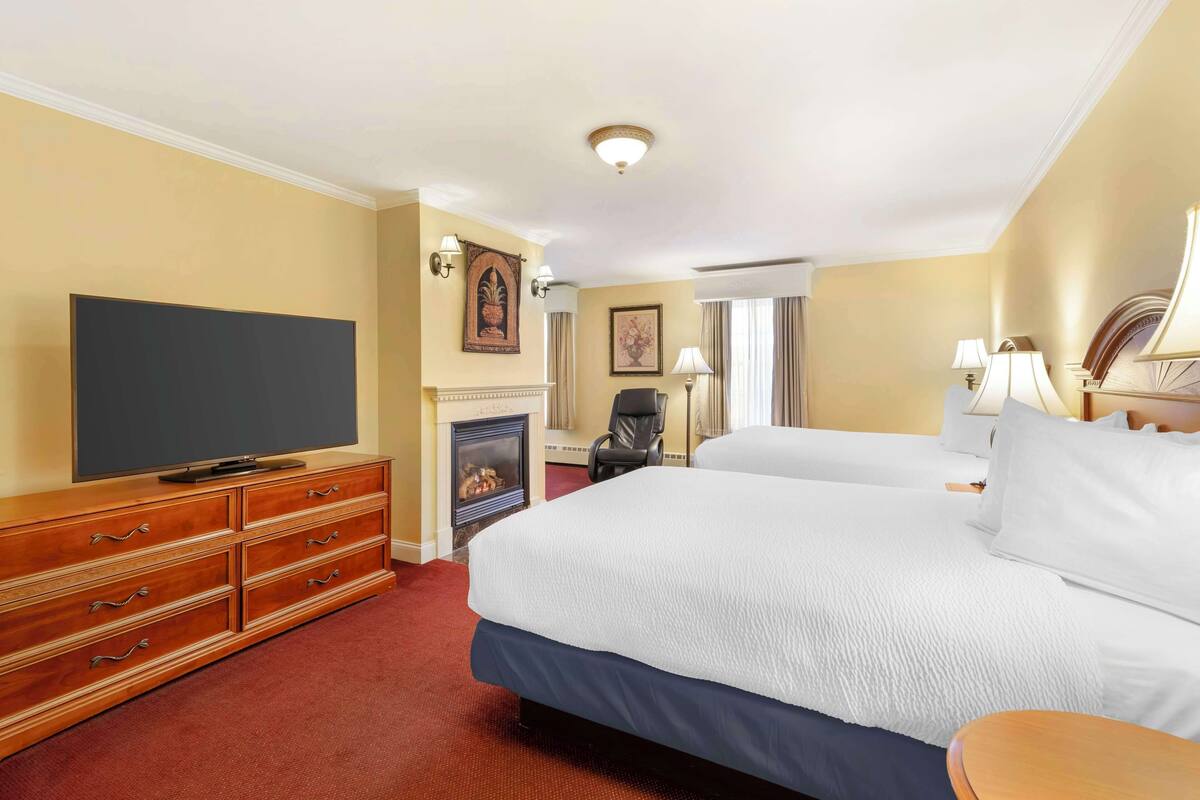 A hotel room with a large bed, a television, a fireplace, and a desk with a chair.