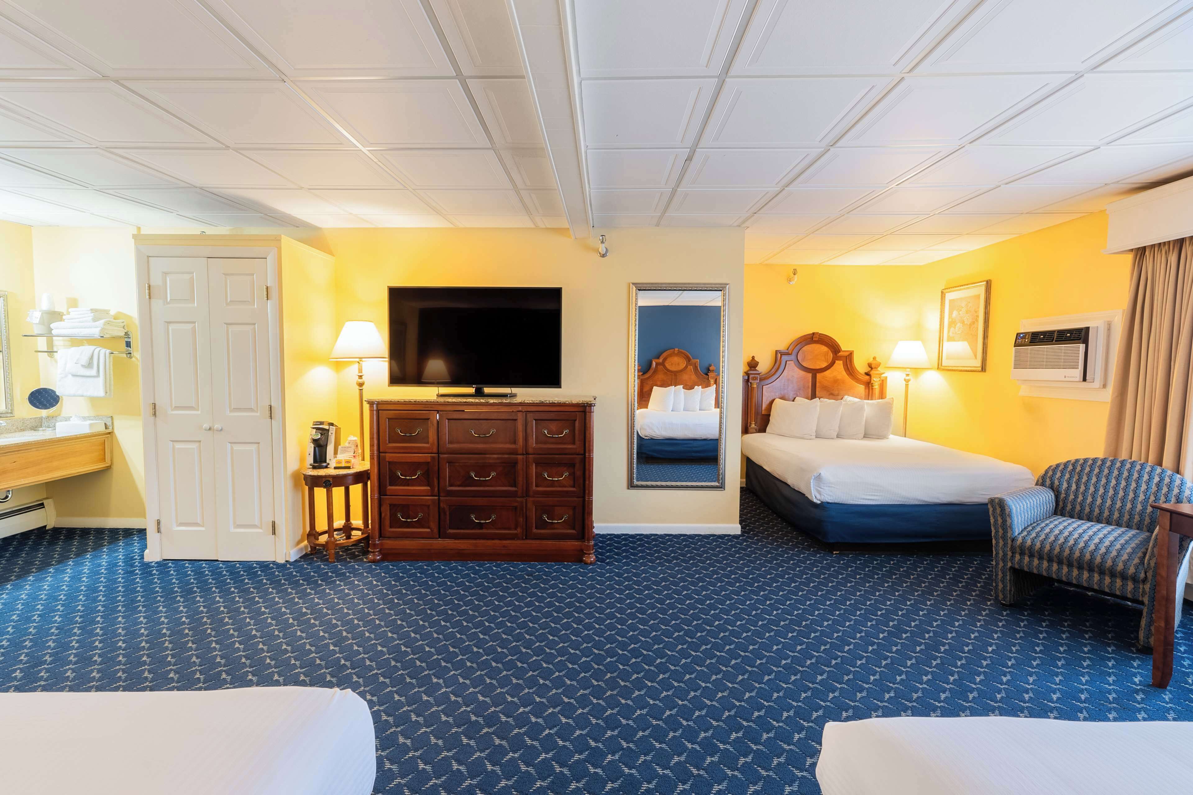 A hotel room with a bed, a dresser, a television, a chair, and a bathroom door.